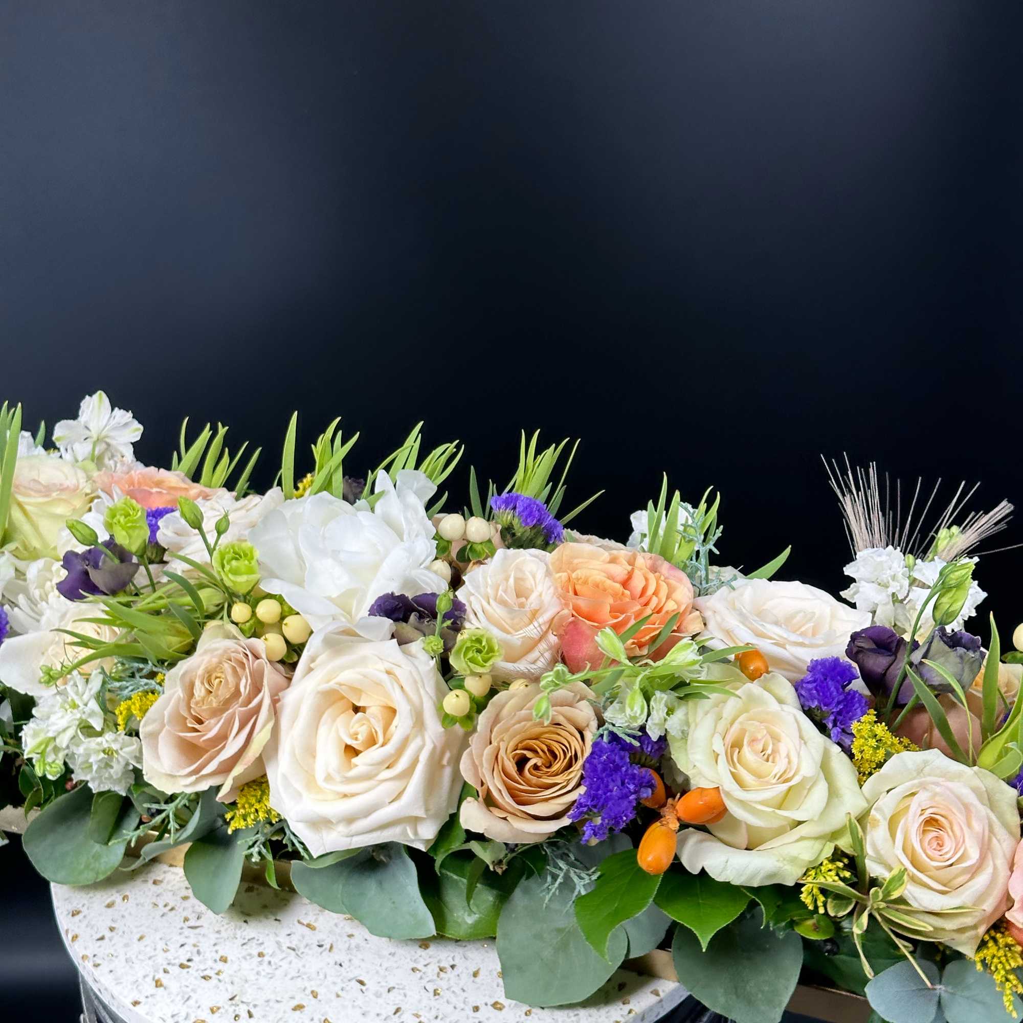 Low floral centerpiece with cream and peach roses, white blooms, and purple accents