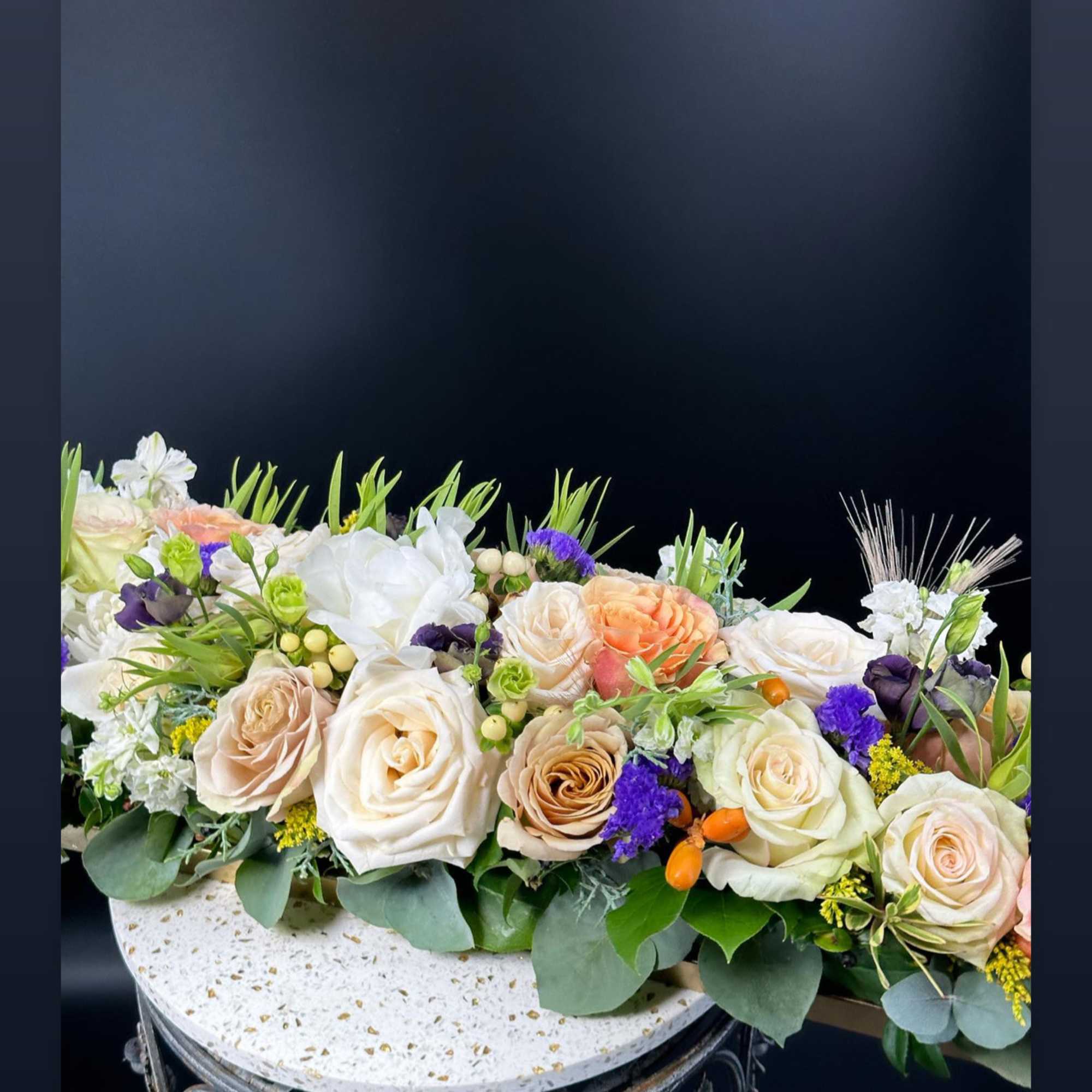 Low floral centerpiece with cream, peach, and purple roses on a round base