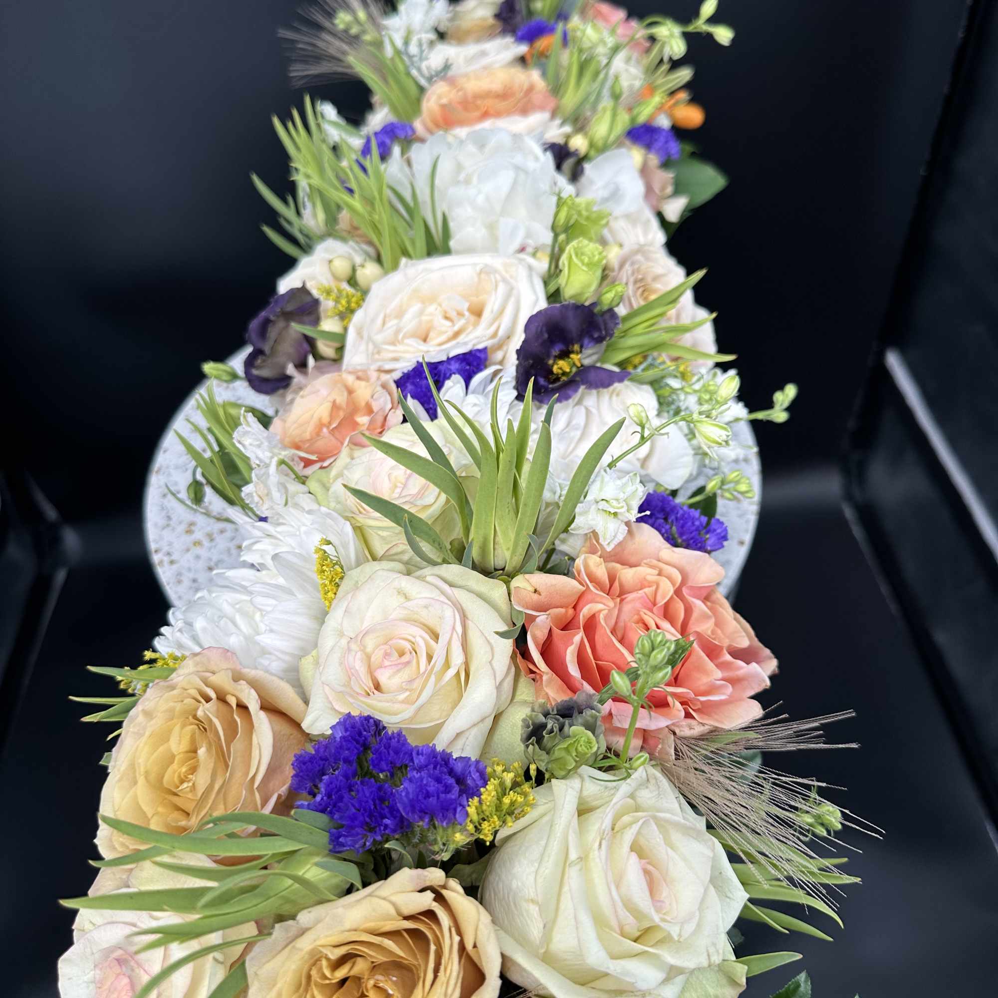 Tall floral arrangement with cream, peach, and purple blooms