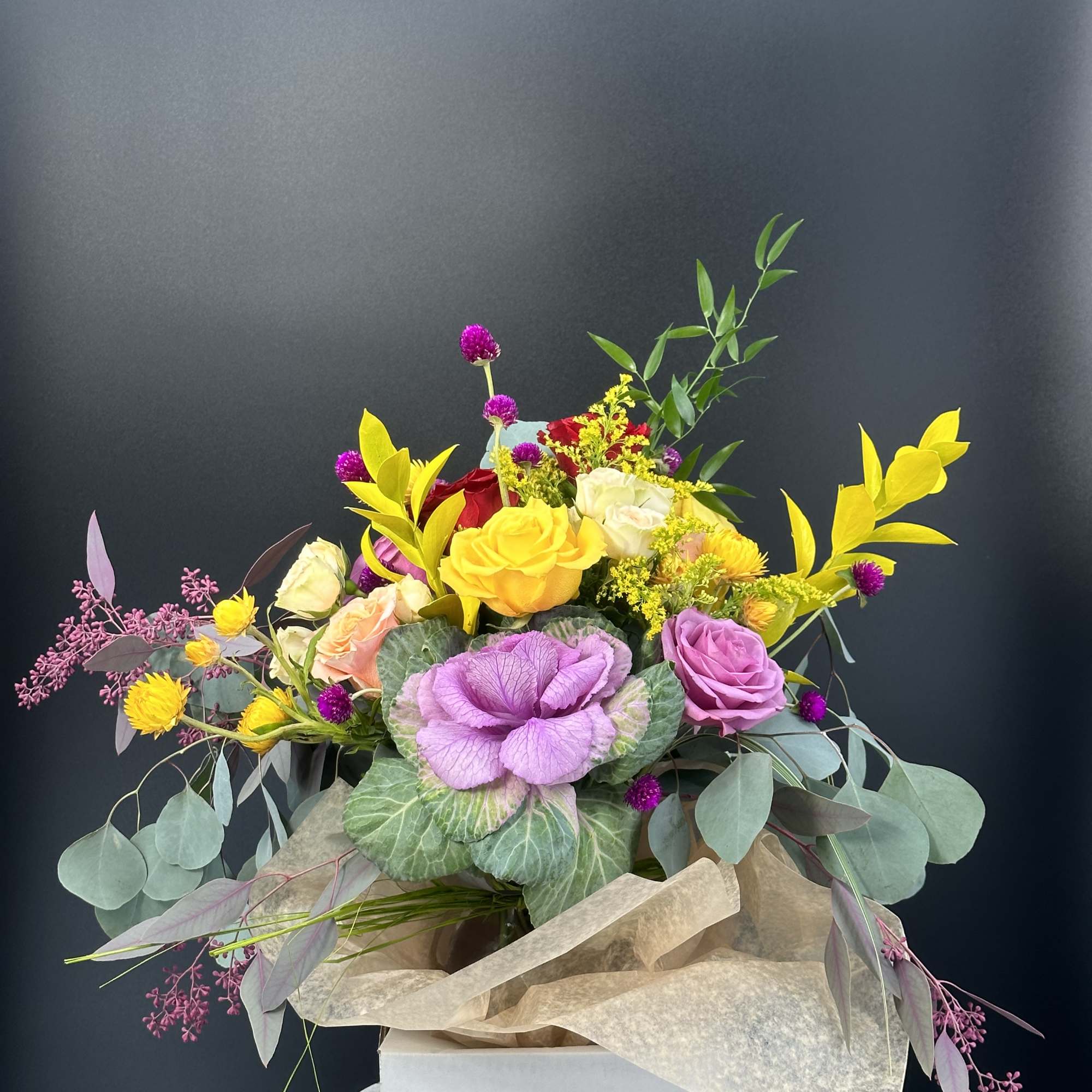 Mixed bouquet with roses, purple cabbage, and yellow accents in a box