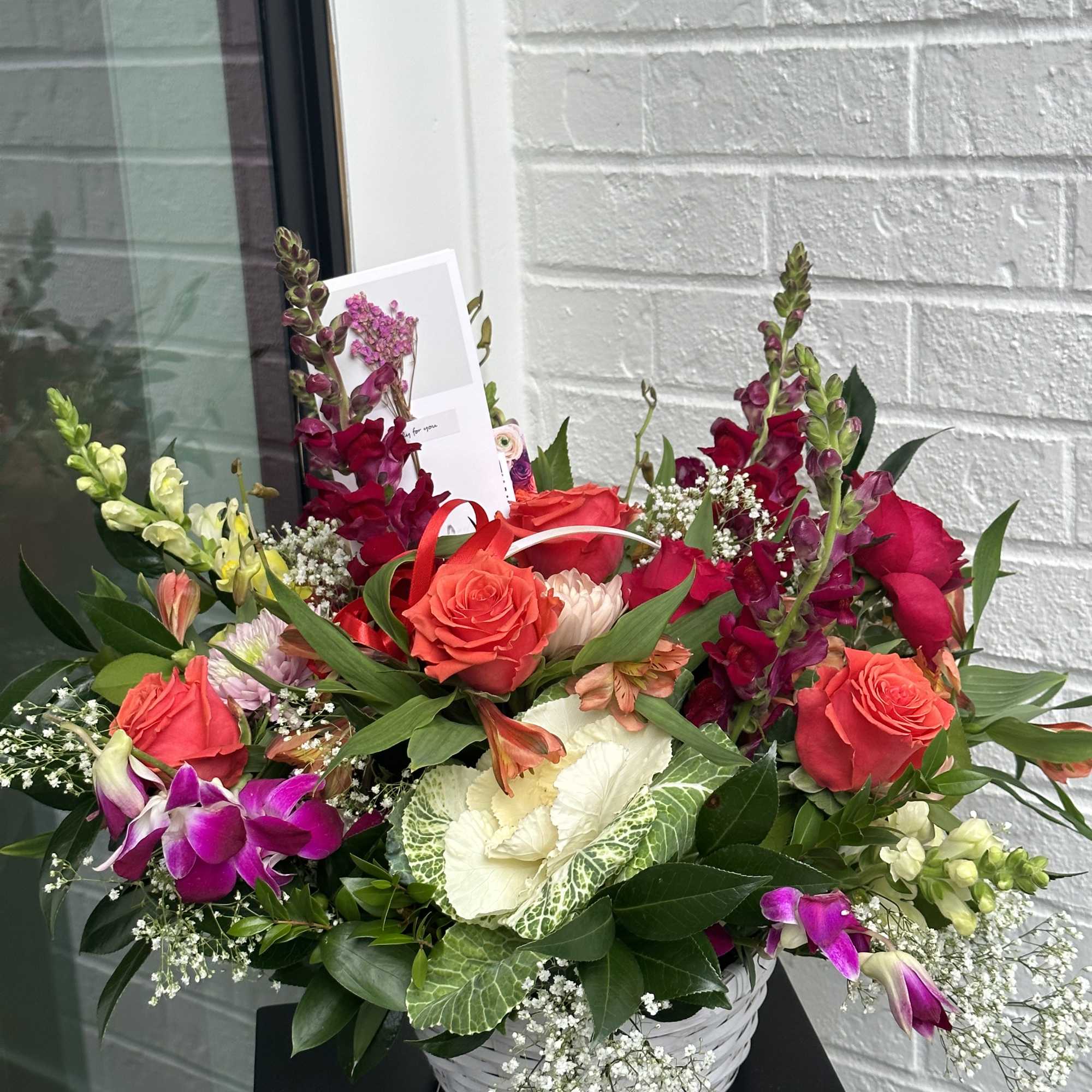 Mixed bouquet of red roses, orchids, and snapdragons in a white basket
