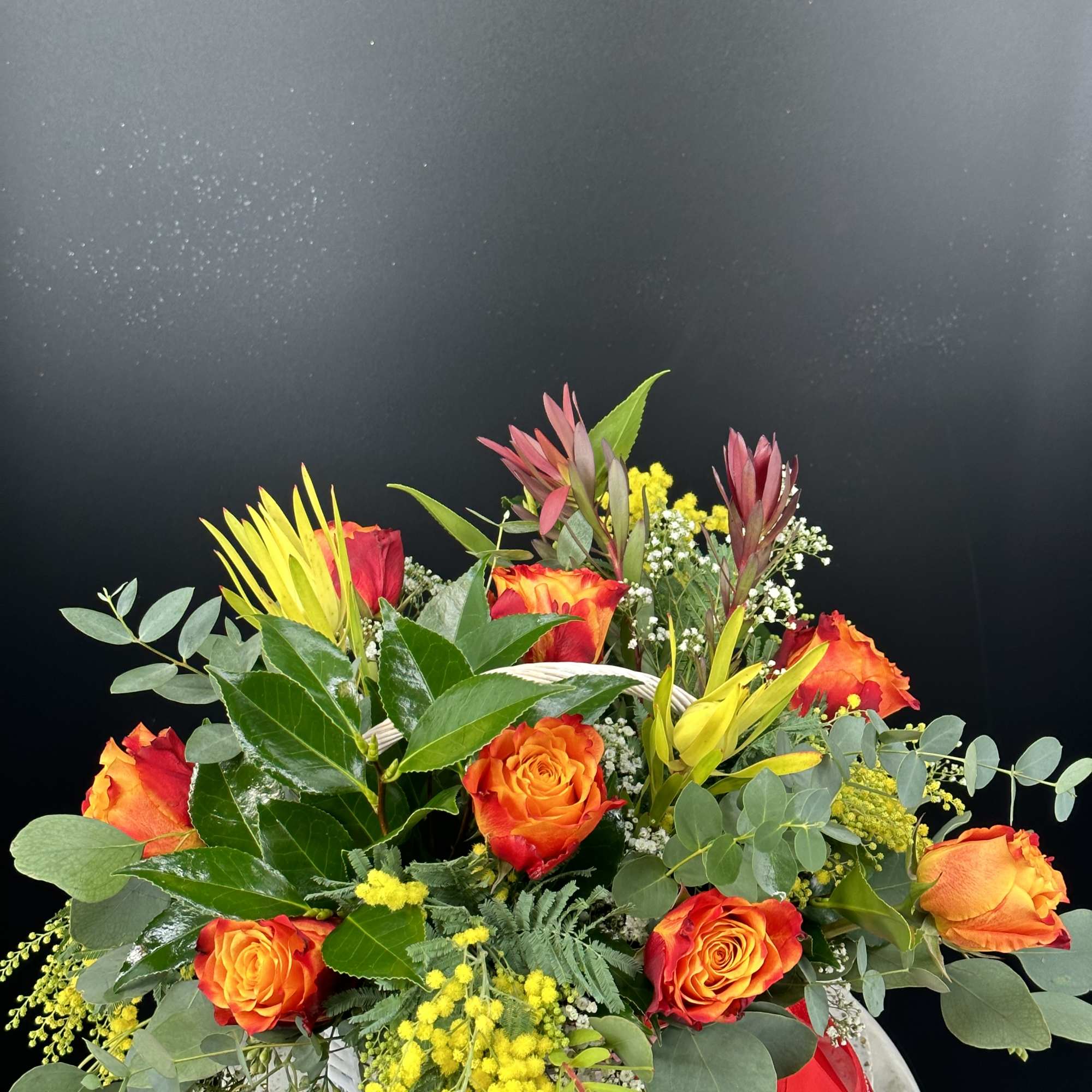 Bouquet of orange and red roses with yellow accents in a white container