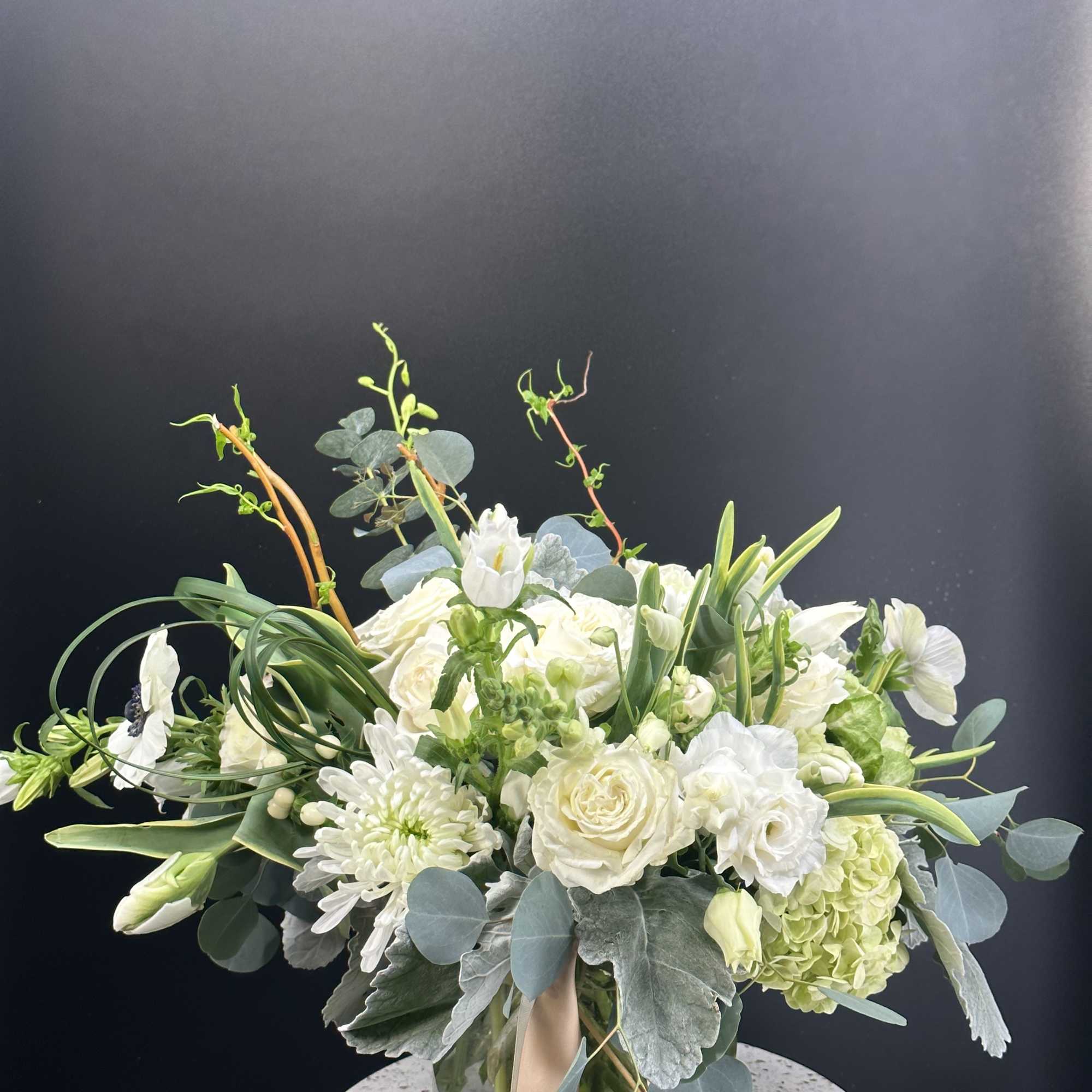 White floral arrangement in a glass vase with eucalyptus and long stems