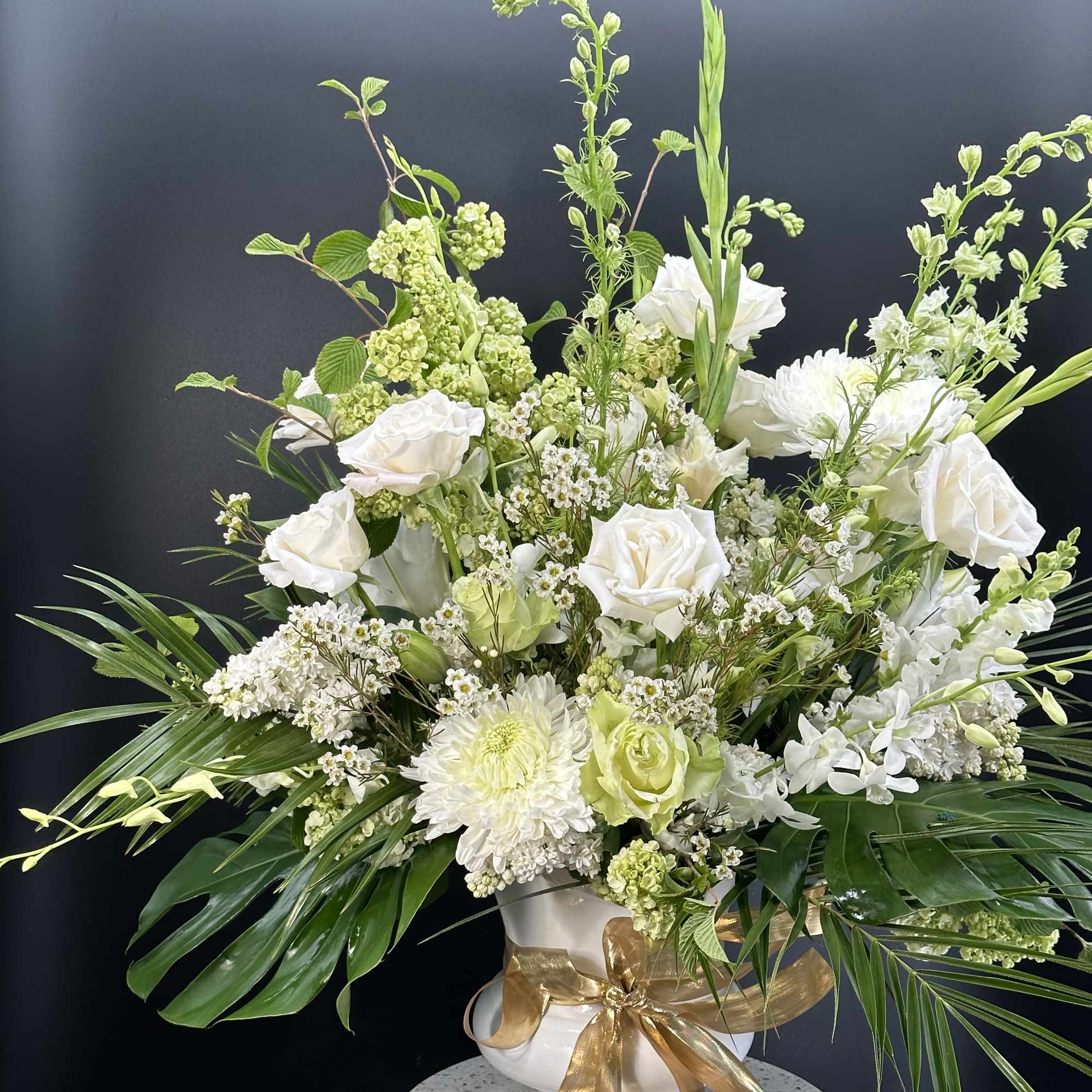 White floral arrangement in a white vase with a gold ribbon