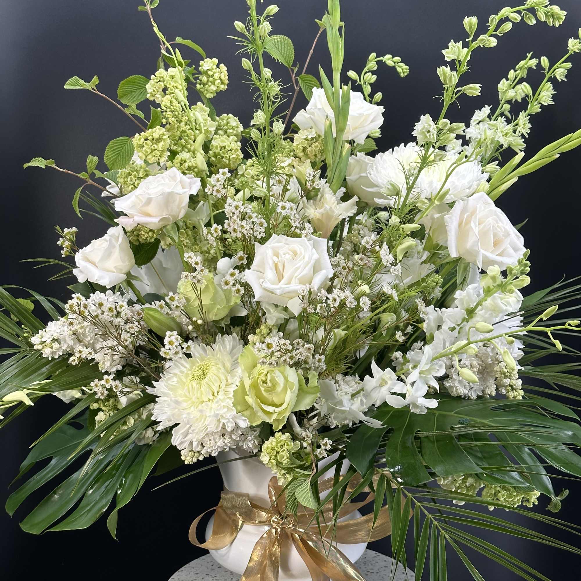 White roses and mixed white flowers arranged in a vase with a gold ribbon