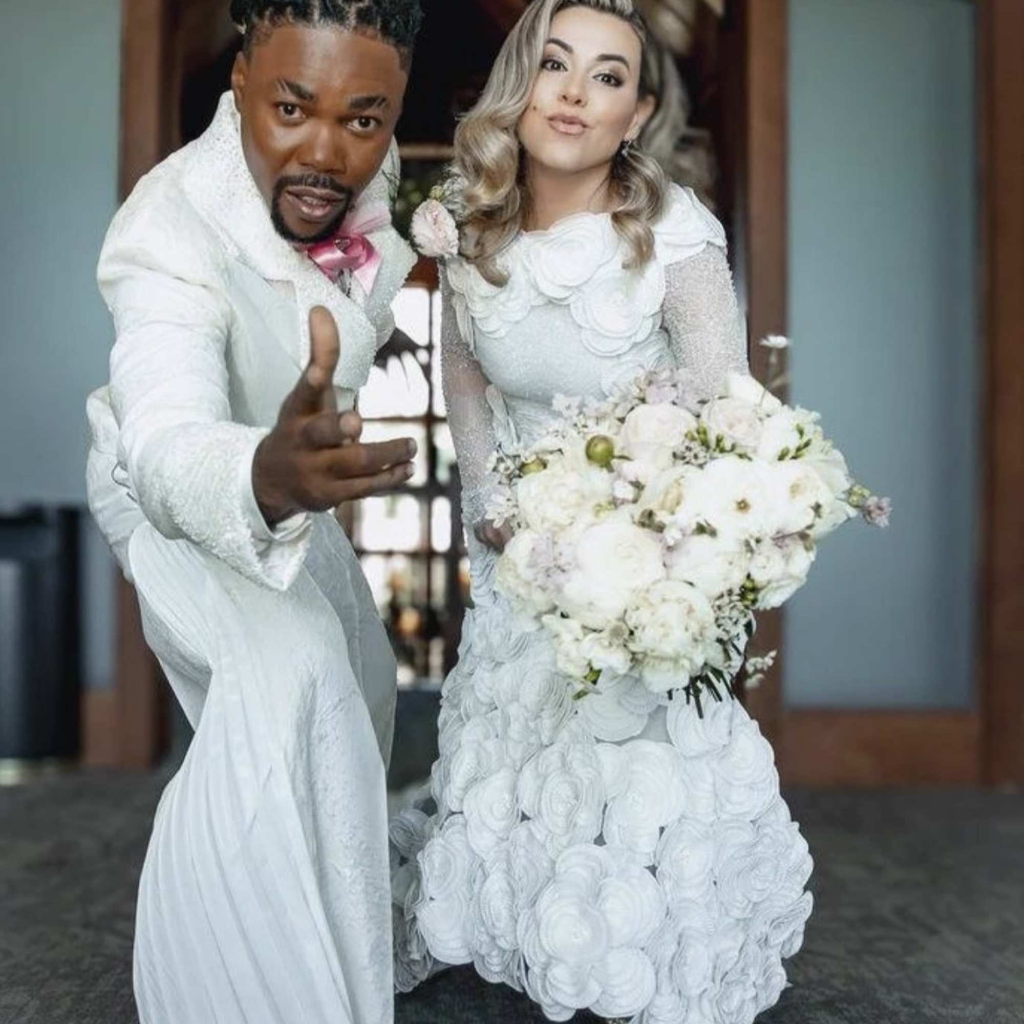 Bride and groom in white outfits, with the bride holding a white bouquet