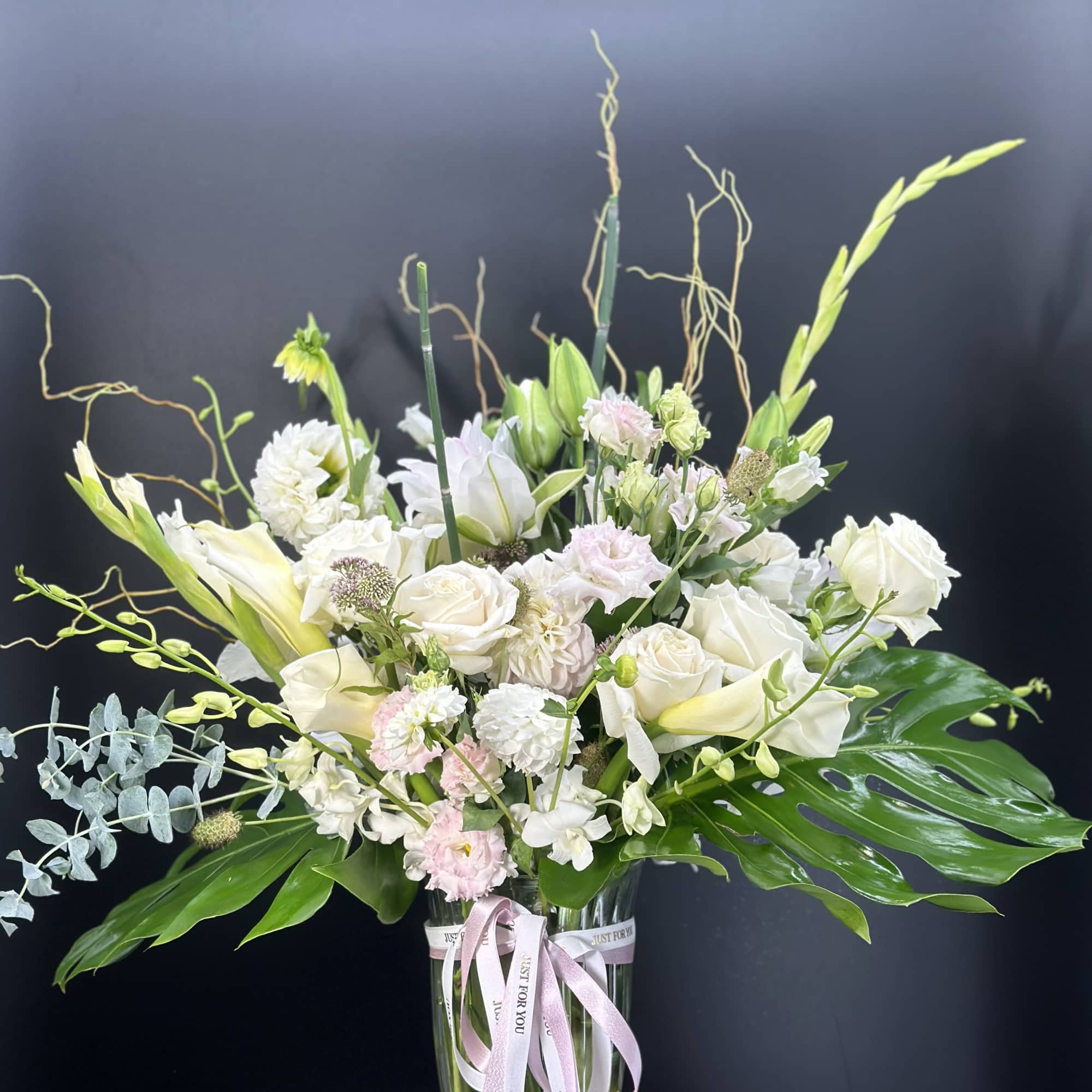 White and pale pink floral arrangement in a clear glass vase with ribbon