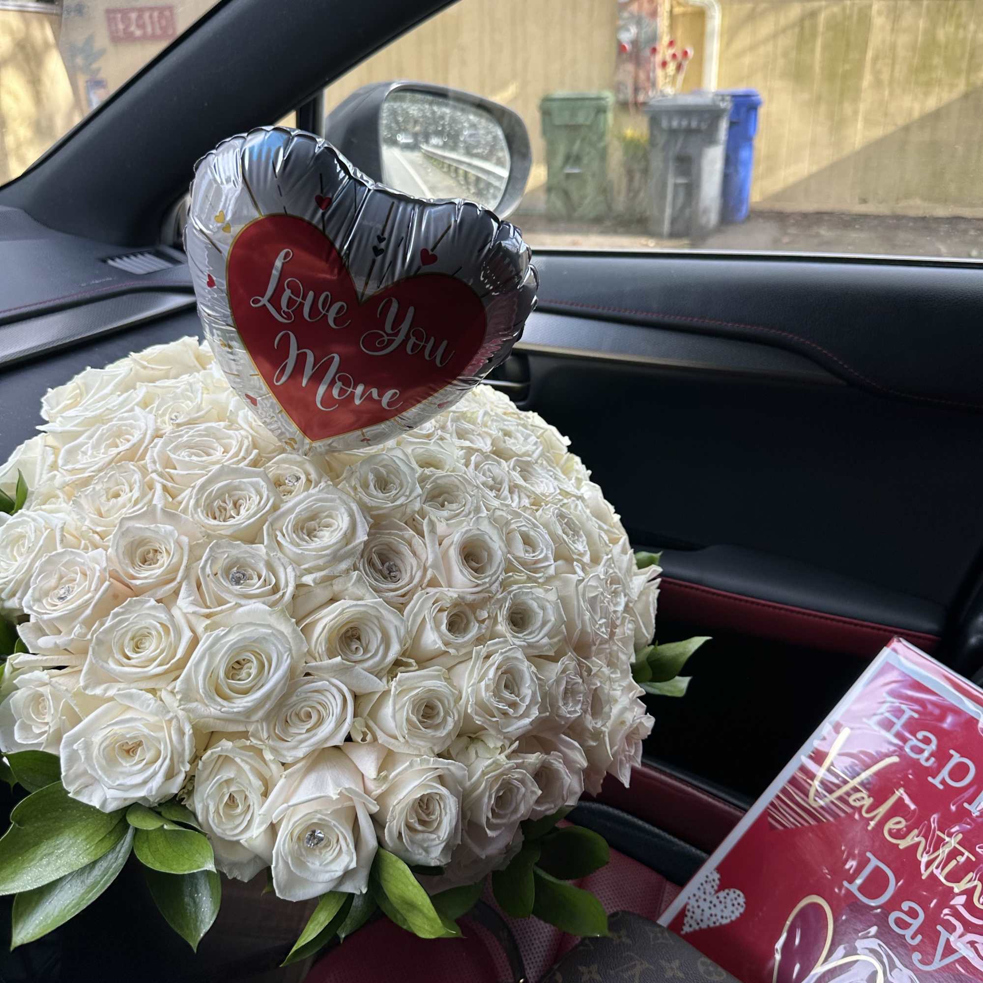 White rose bouquet with a heart-shaped "Love You More" balloon