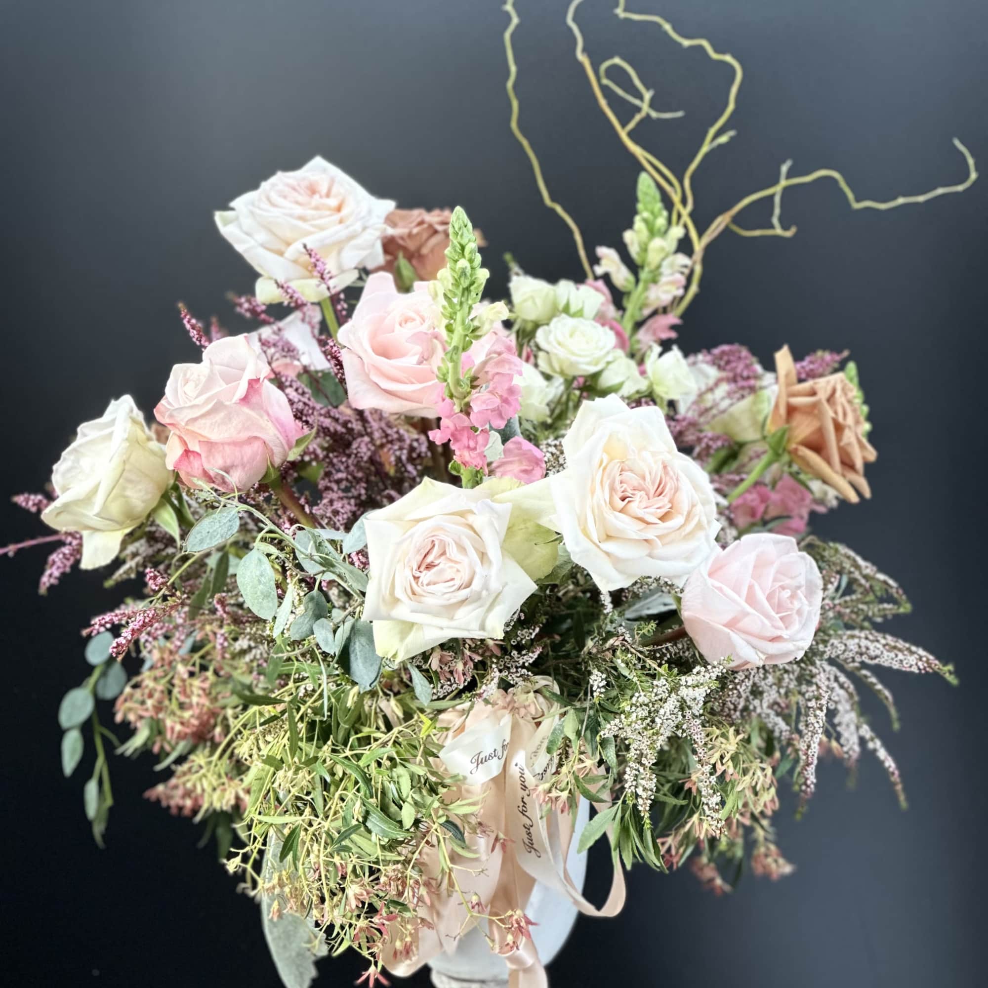 Large pastel rose and snapdragon arrangement with trailing greenery in a white urn vase