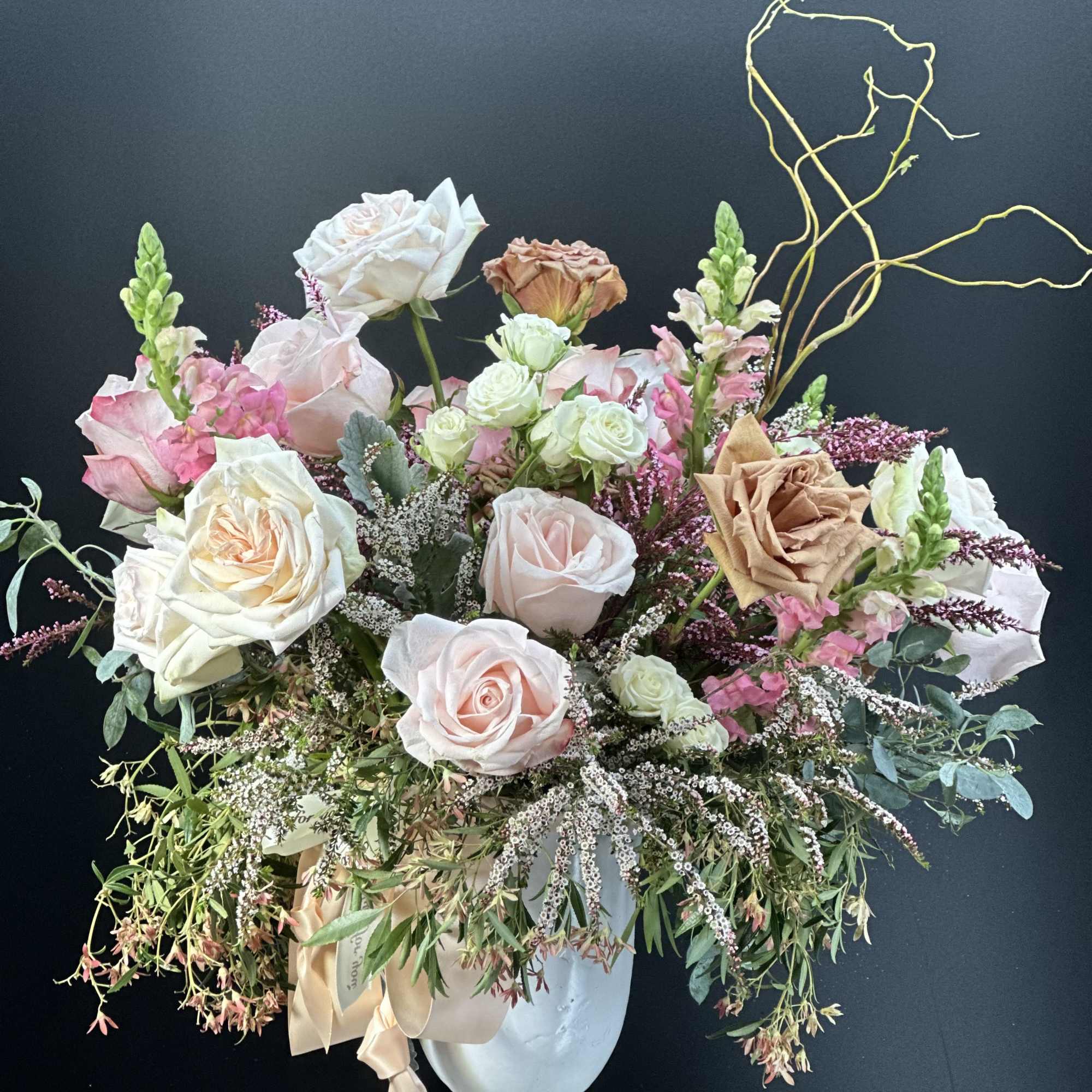 Large pastel arrangement of roses and snapdragons in a white urn on a pedestal.