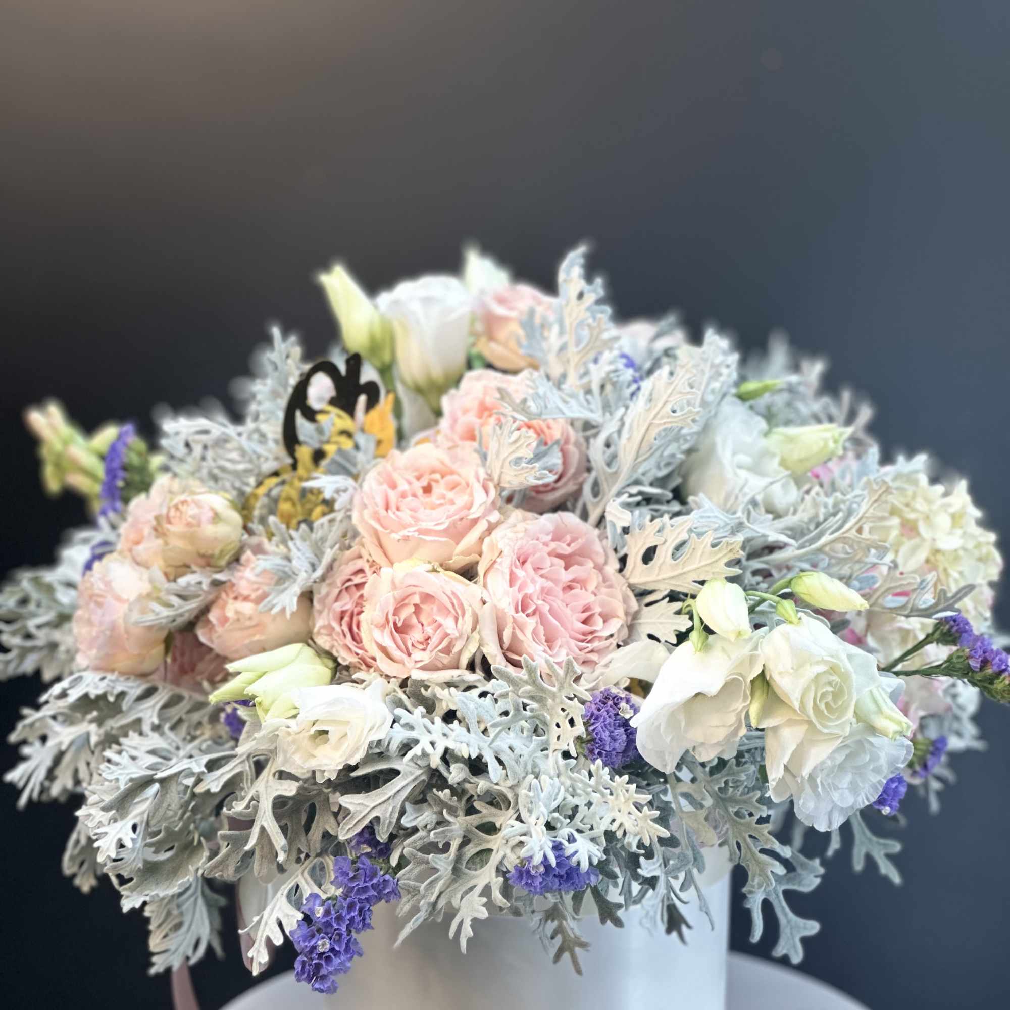Pink and white roses arranged in a white hatbox with silver foliage
