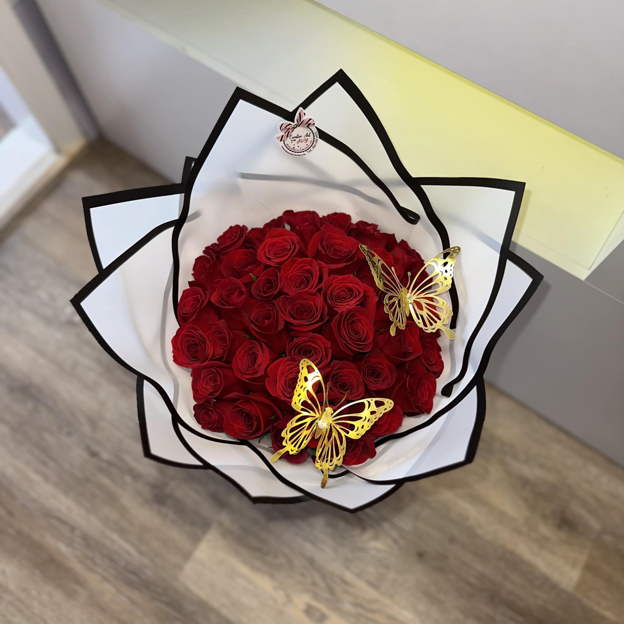 Bouquet of red roses wrapped in white paper with black trim and gold butterfly accents