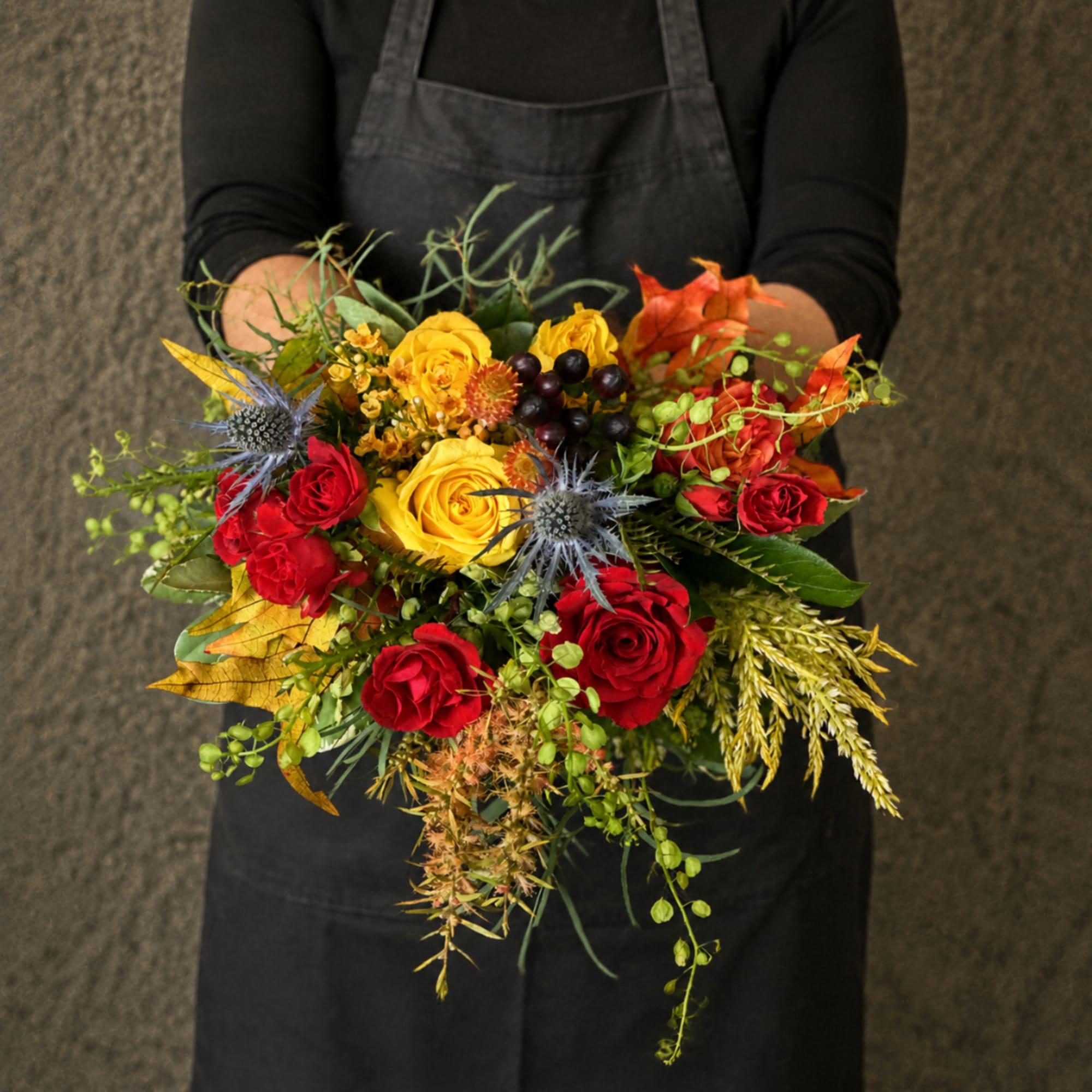 Handheld bouquet of red and yellow roses with autumn foliage