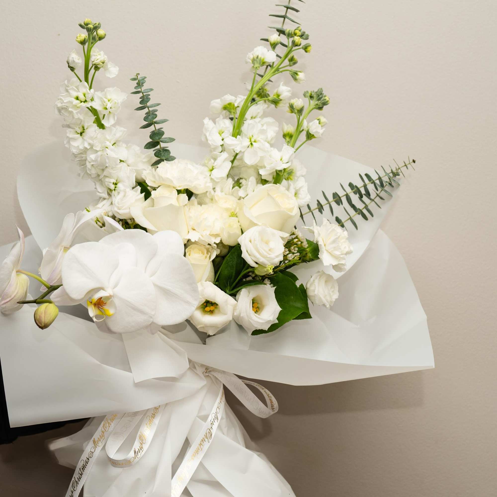 White bouquet with orchids, roses, and tall white blooms wrapped in paper