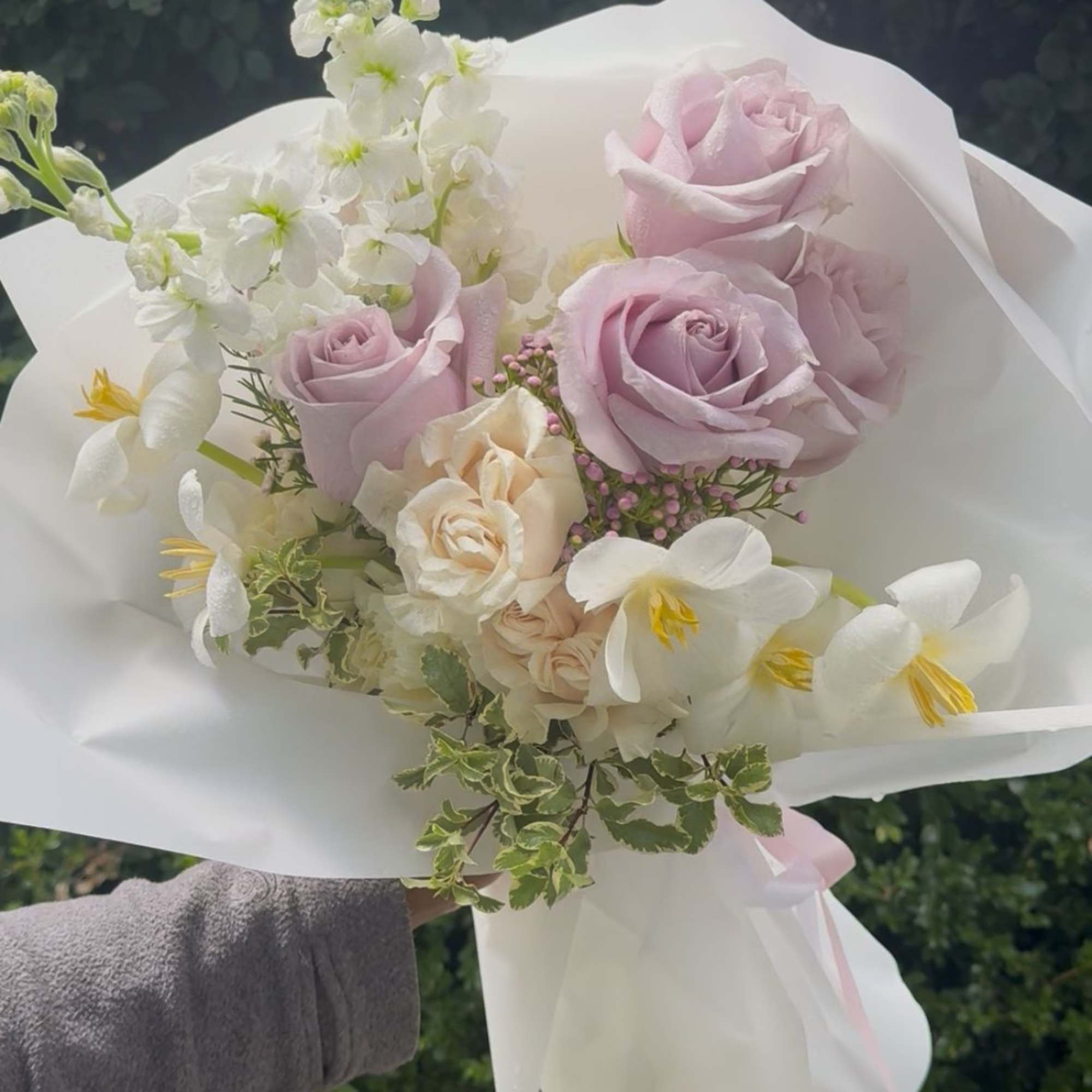 Handheld bouquet of pale pink and white flowers wrapped in white paper