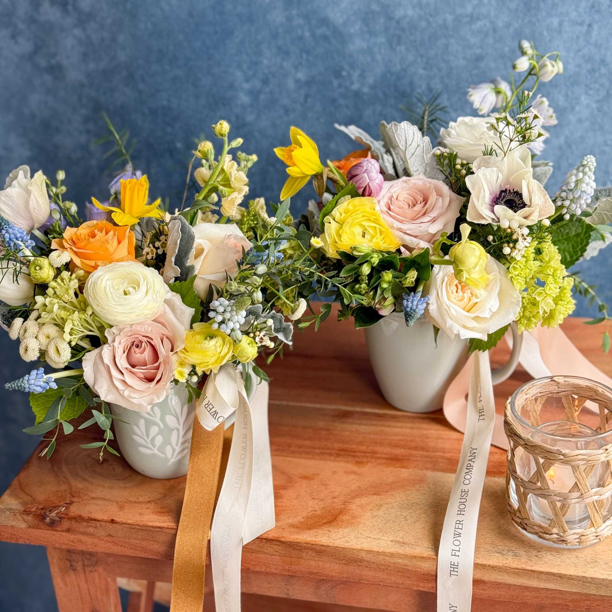 Two mixed flower arrangements in white mugs on a wooden table