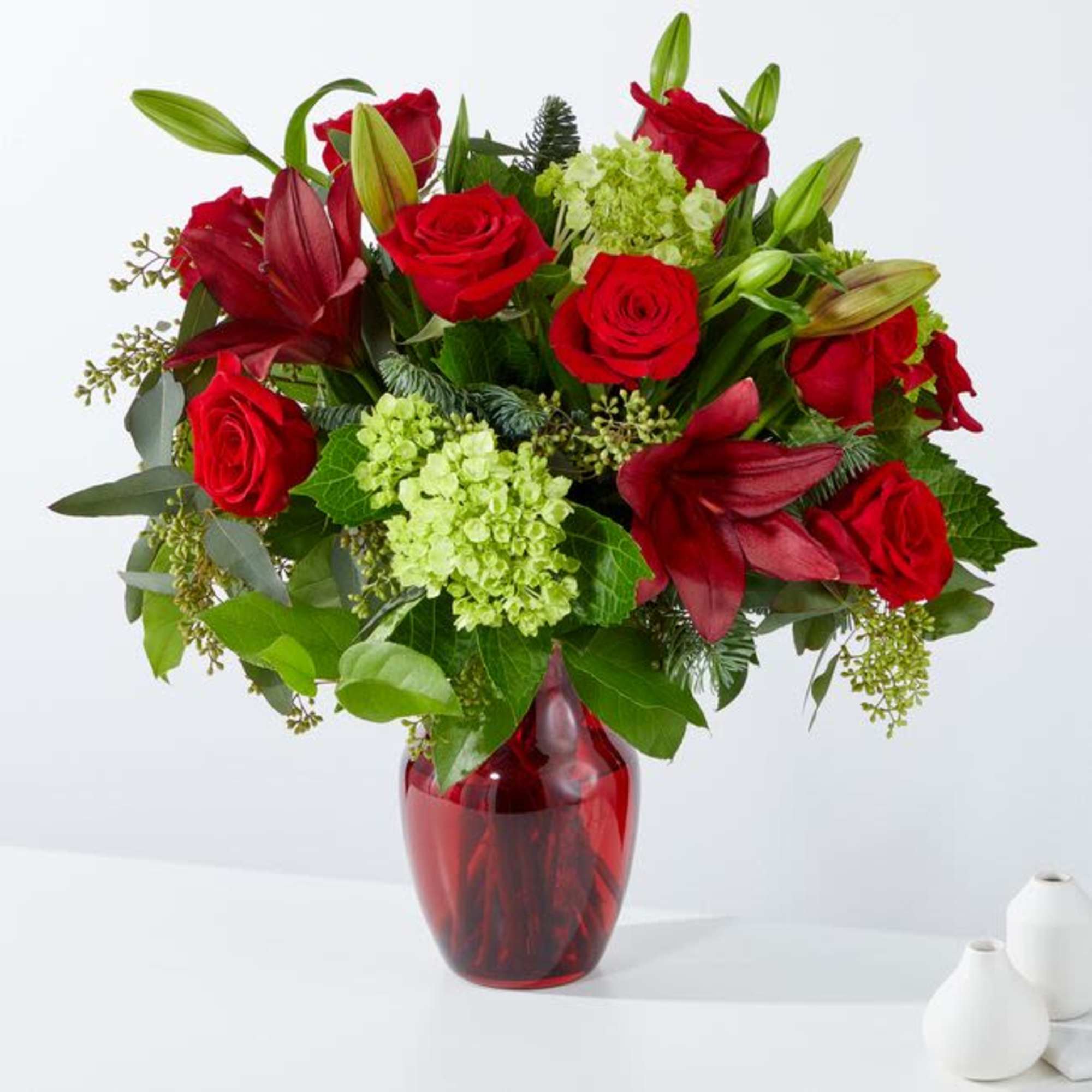 Red roses and lilies arranged in a red glass vase