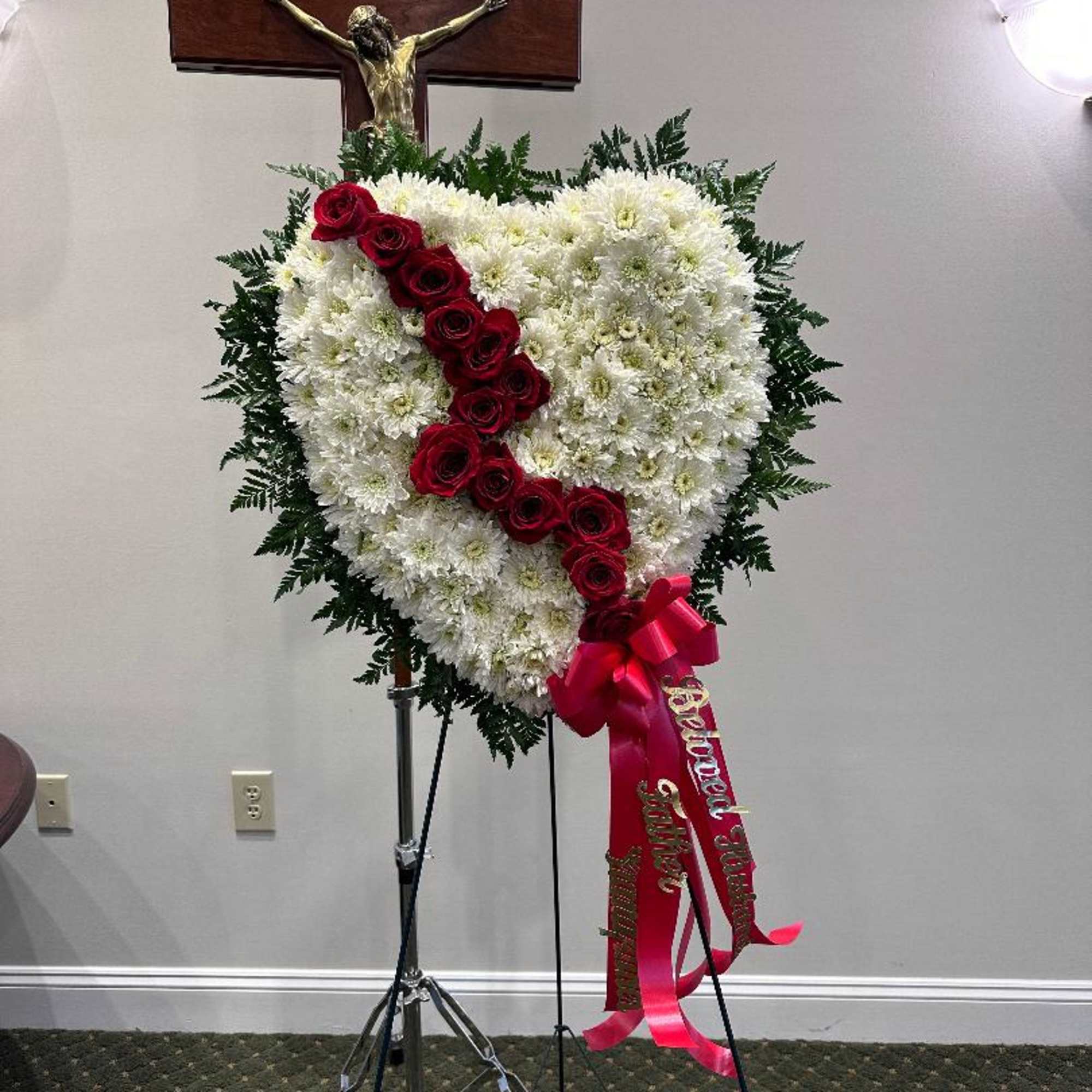 Heart-shaped funeral spray of white flowers with red roses and a ribbon