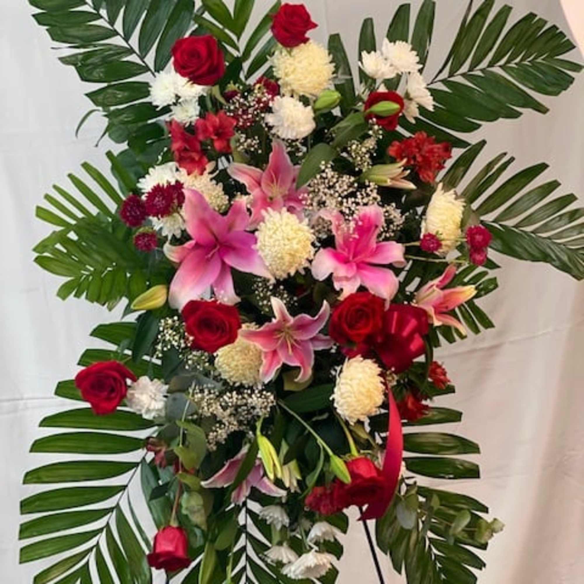 Standing floral spray with red roses, pink lilies, and white blooms