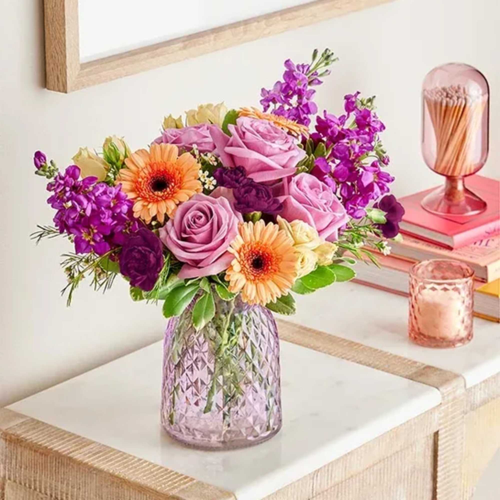 Bouquet of pink roses, gerbera daisies, and purple flowers in a textured glass vase