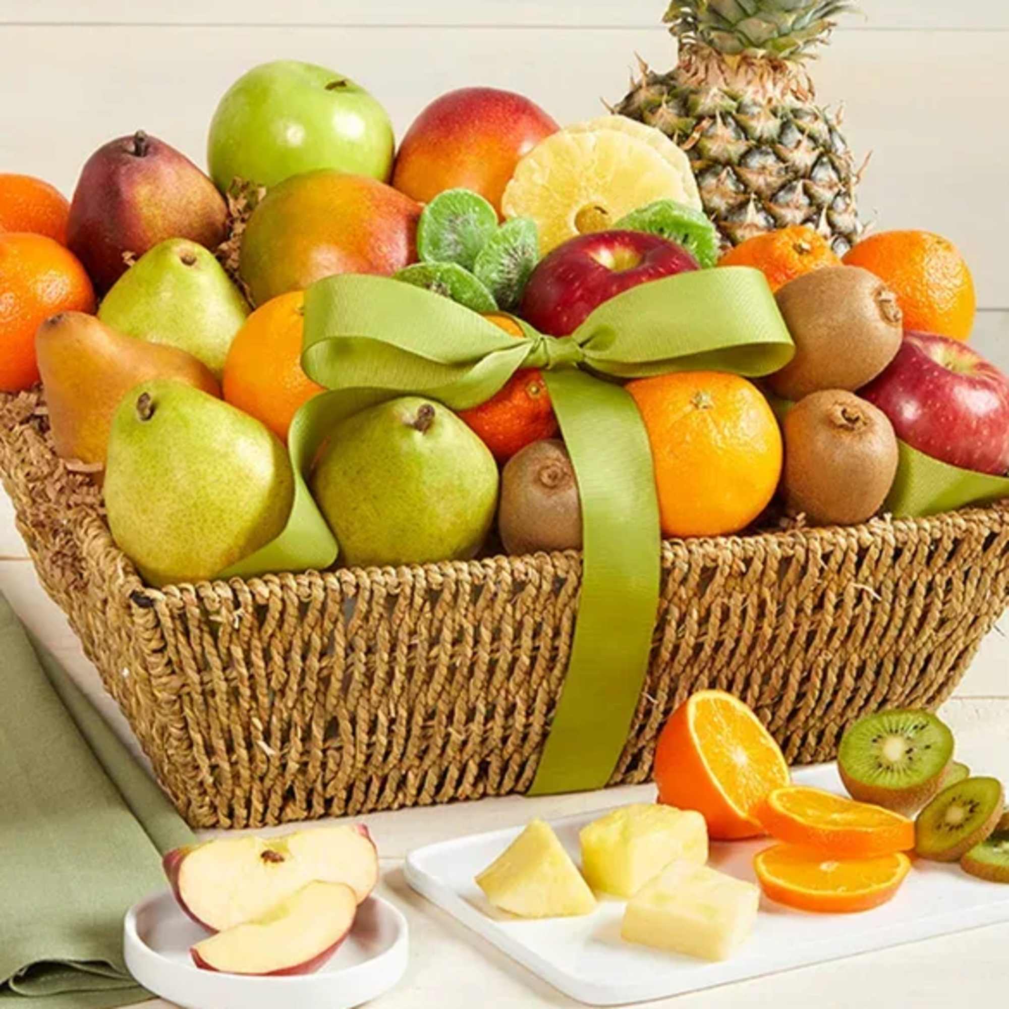 Fruit basket with apples, pears, oranges, kiwi, and pineapple tied with a green ribbon