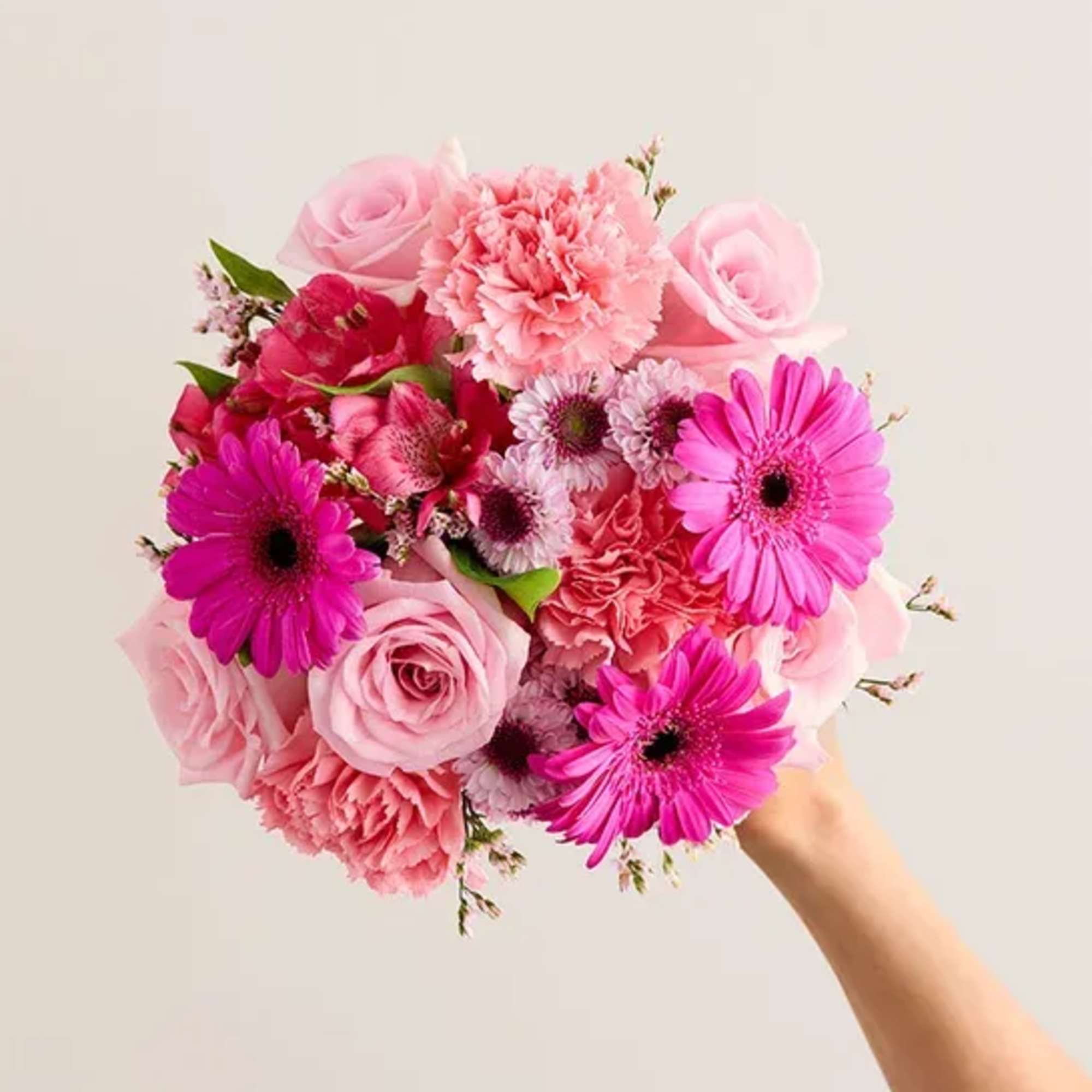 Handheld bouquet of pink roses, carnations, and gerbera daisies