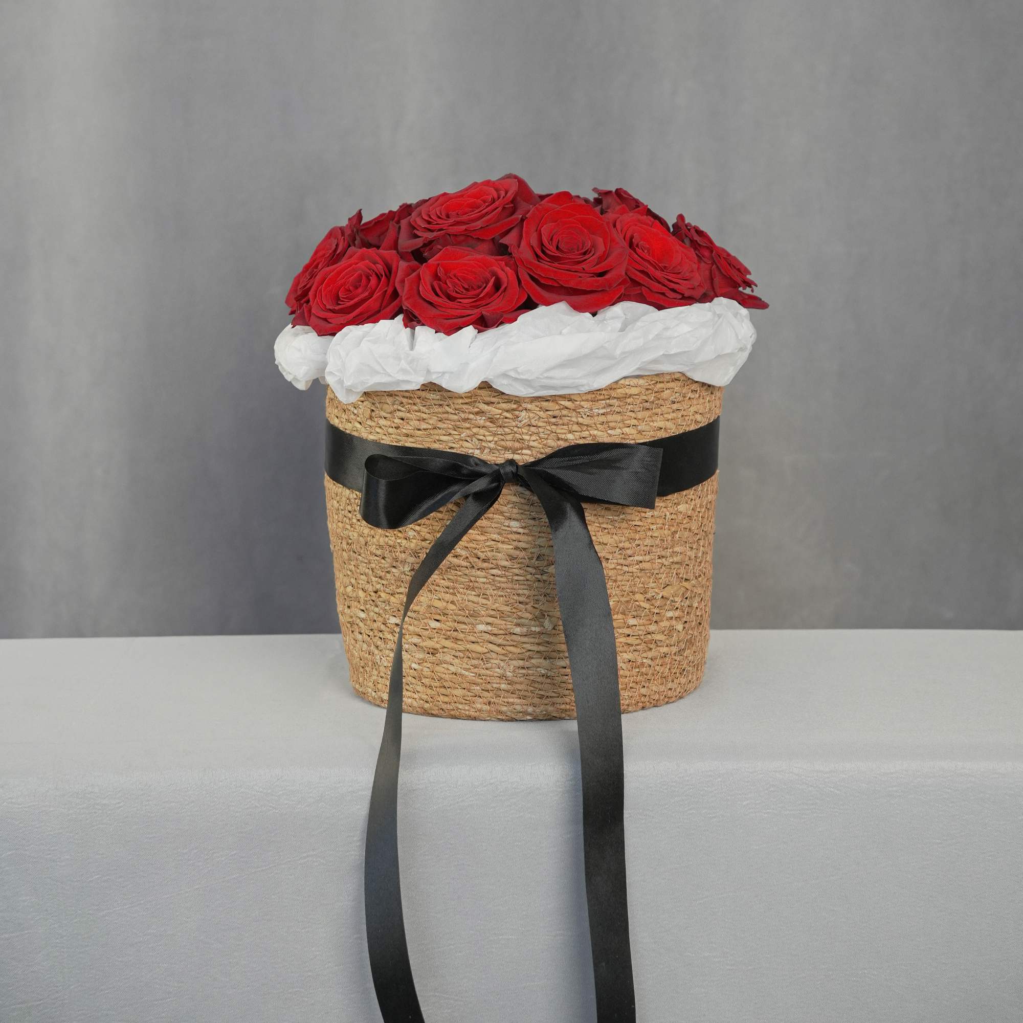 Red roses arranged in a woven hatbox with a black ribbon
