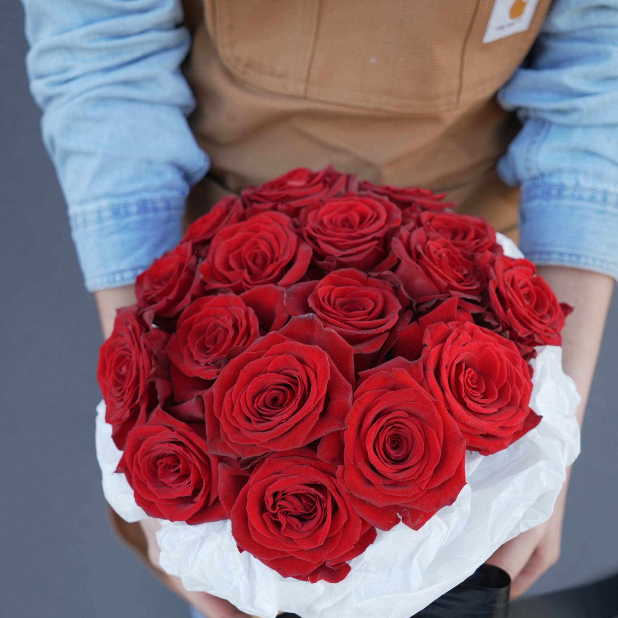 Handheld bouquet of red roses wrapped in white paper with a black ribbon