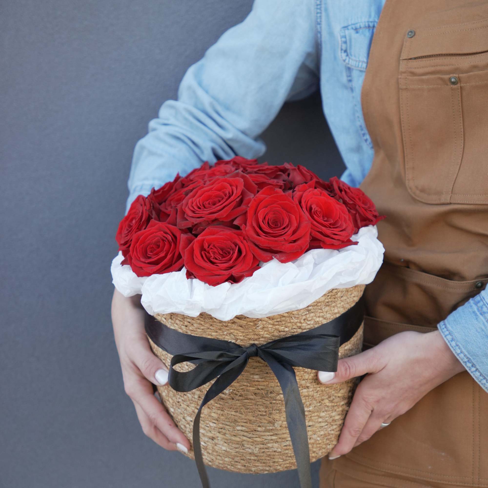 Round box of red roses with white tissue and a black ribbon