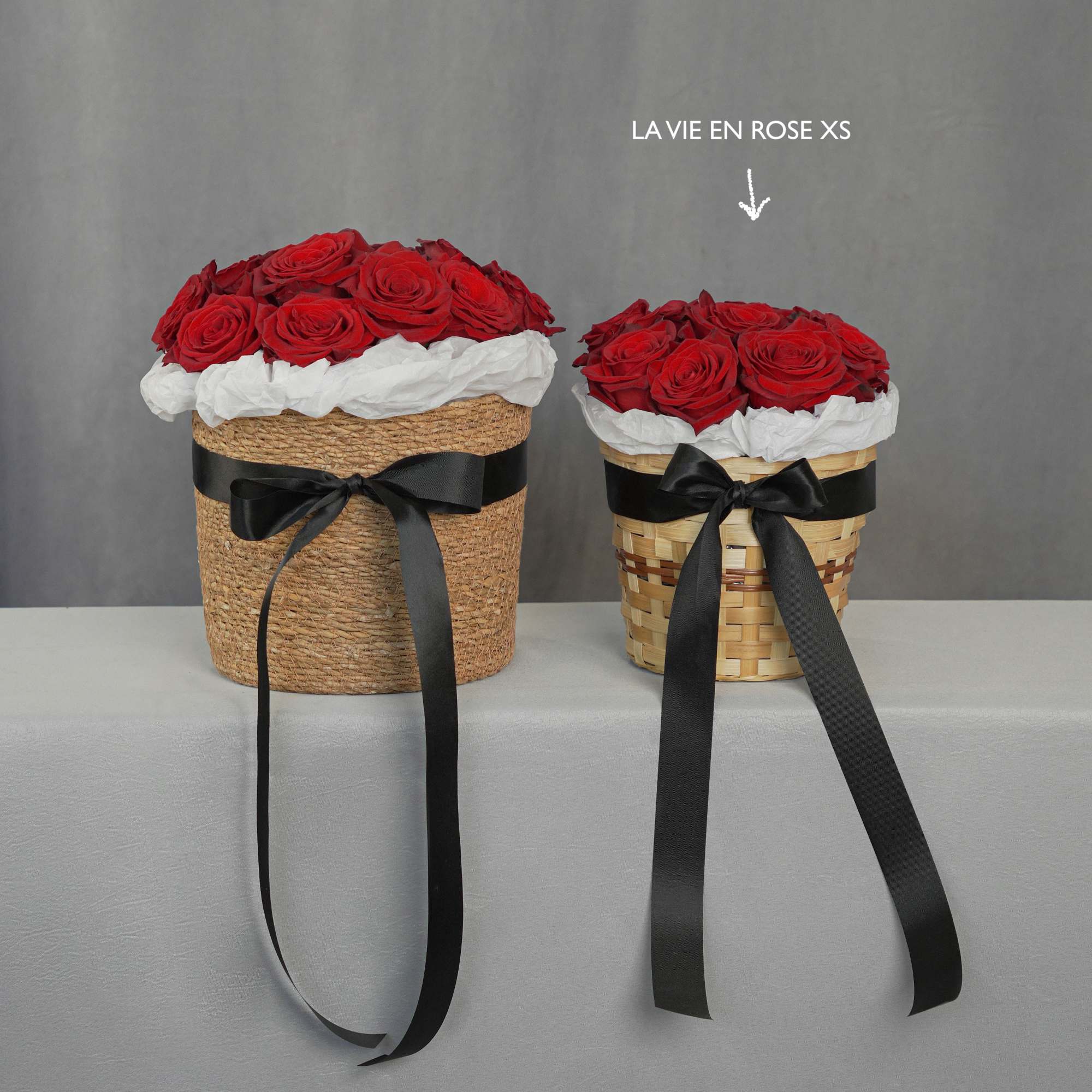 Two red rose arrangements in woven baskets with black ribbons