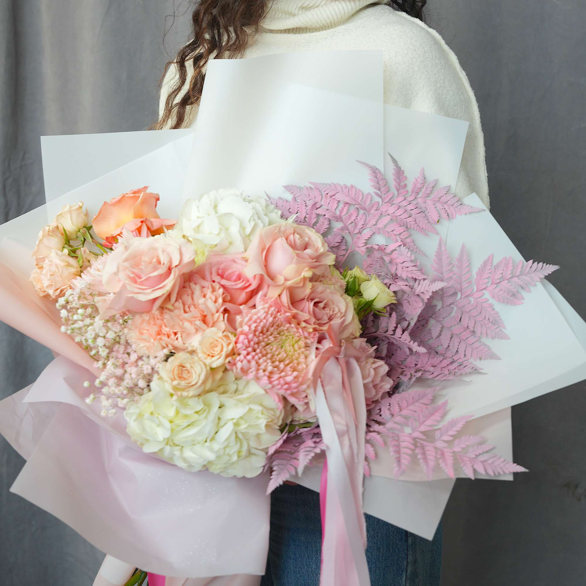 Pastel bouquet of roses, hydrangeas, and pink fern-like foliage wrapped in paper