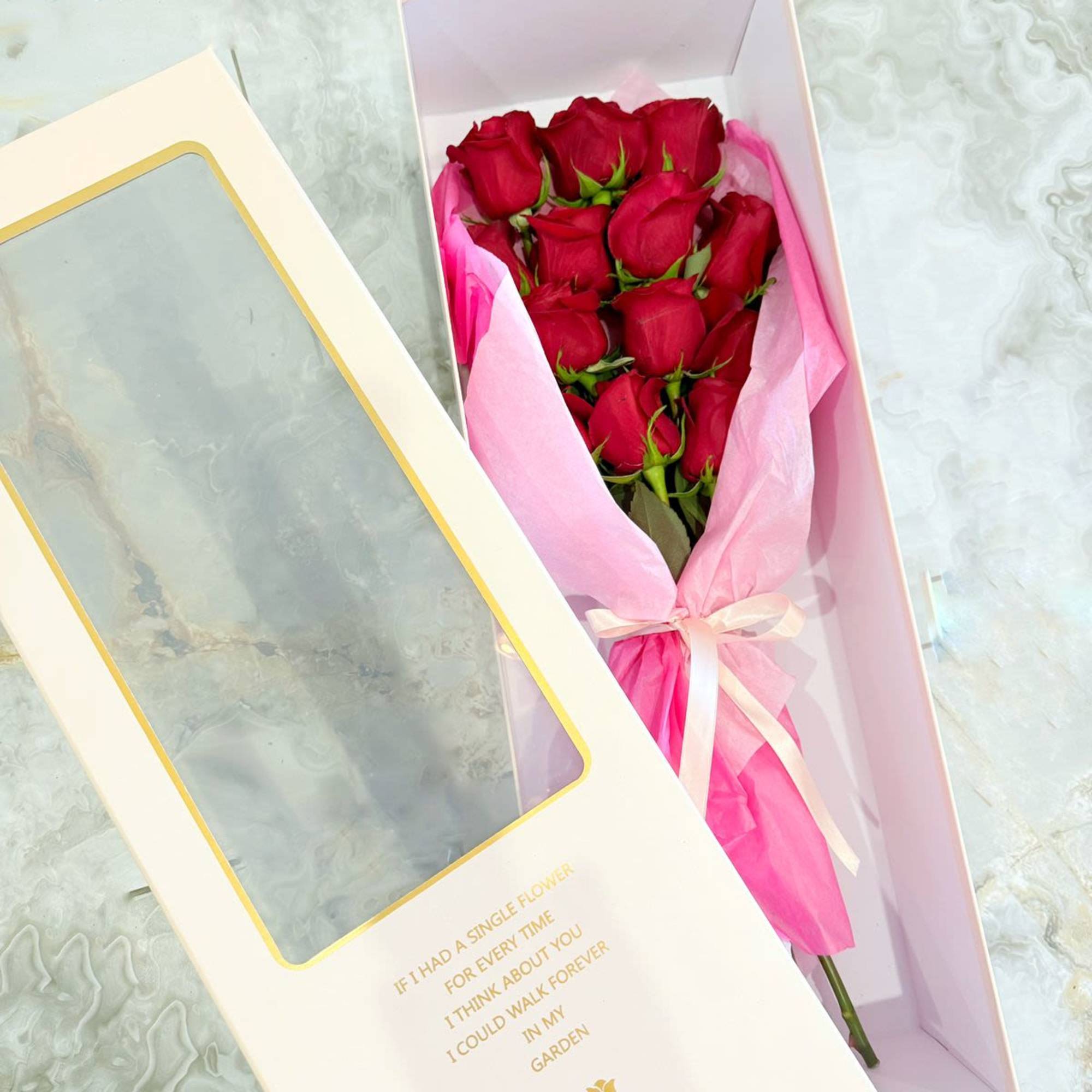 Boxed bouquet of red roses wrapped in pink tissue with a ribbon