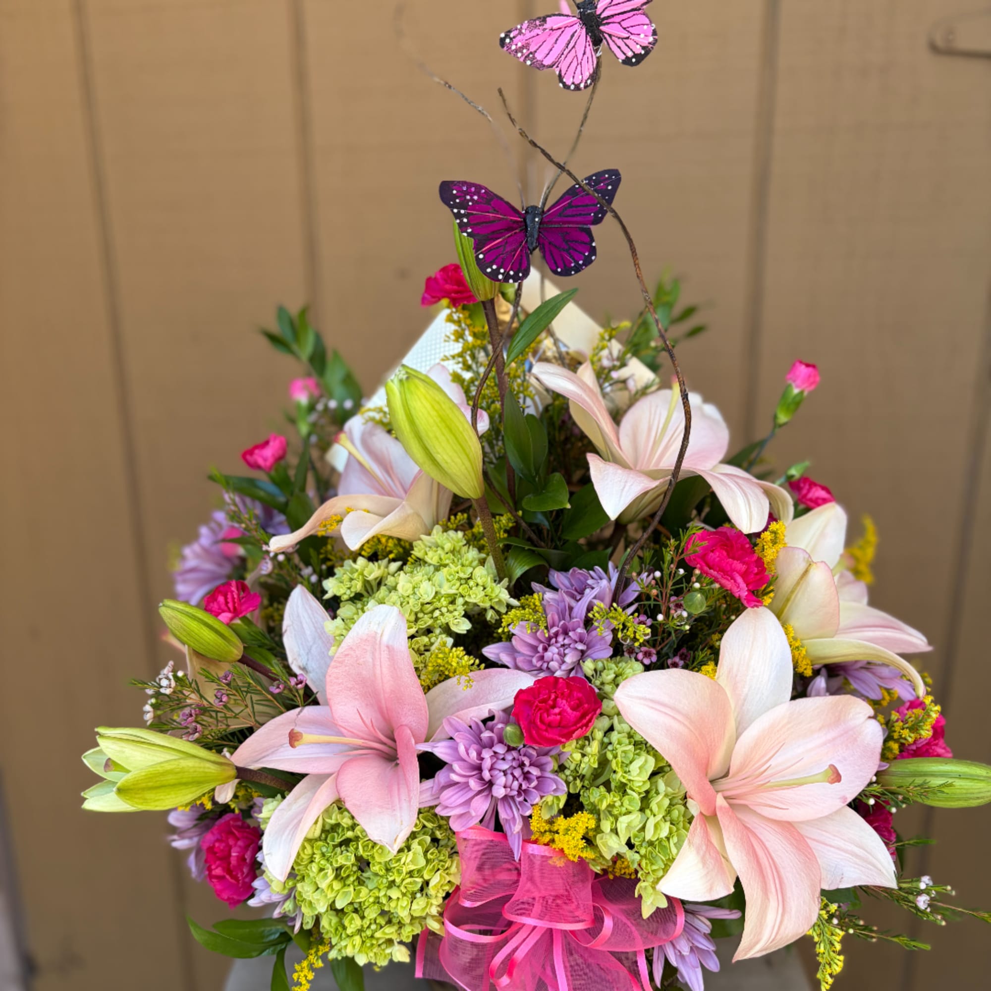 Mixed bouquet with pink lilies, purple flowers, and butterfly picks in a pink ribbon wrap