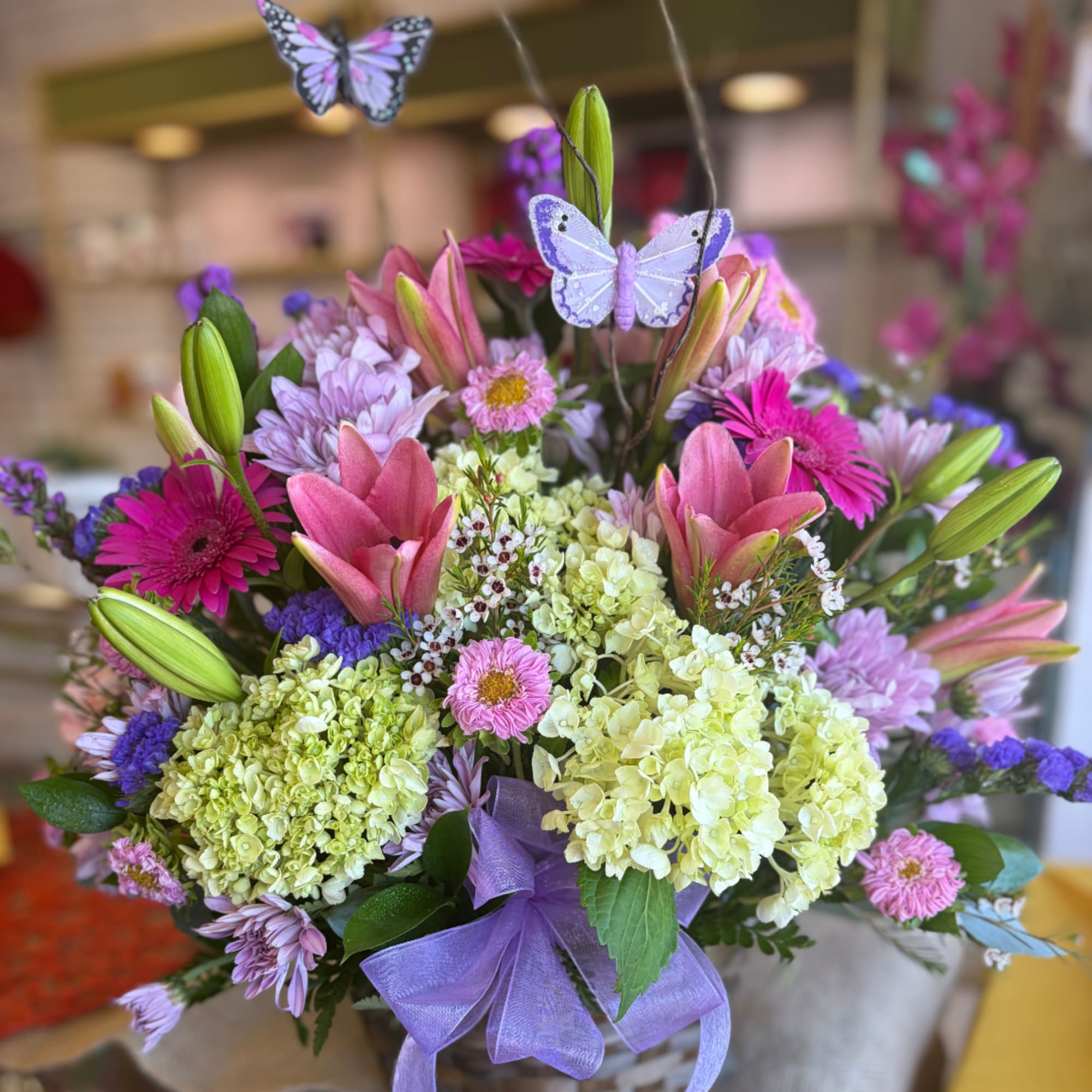 Mixed bouquet with pink lilies, purple daisies, and pale hydrangeas in a basket