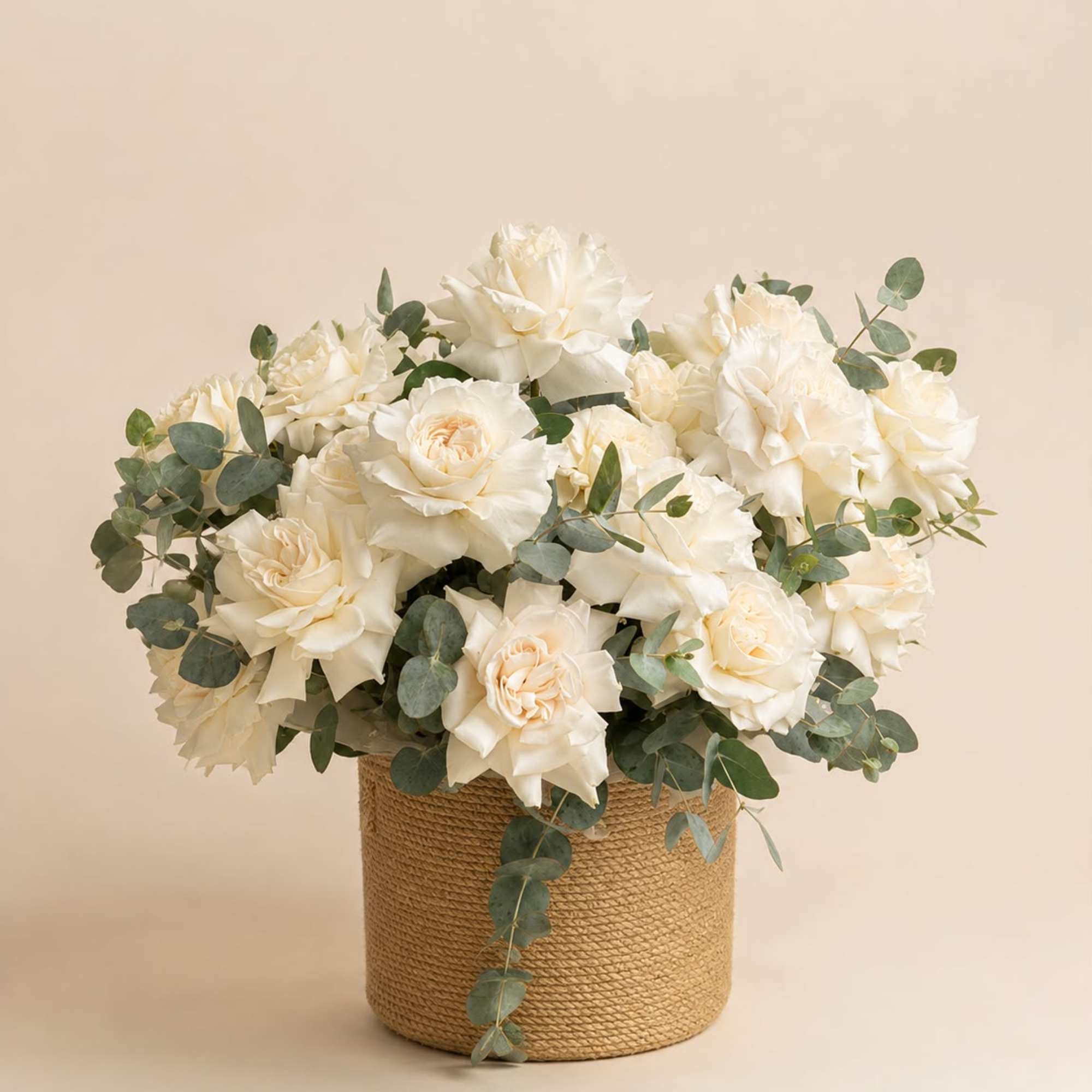 White roses arranged in a woven basket with eucalyptus
