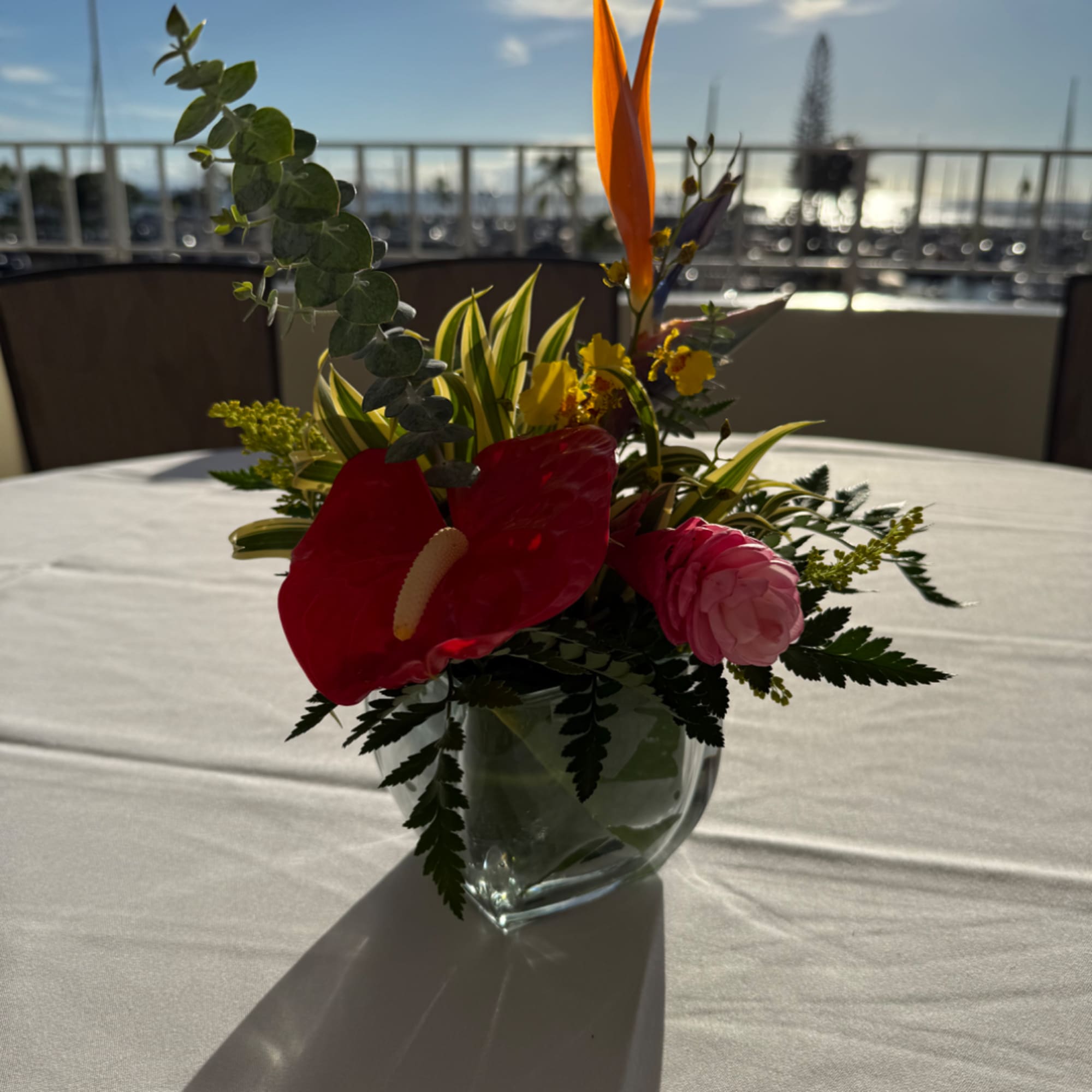 Mixed tropical arrangement in a clear glass vase with red anthurium and pink blooms