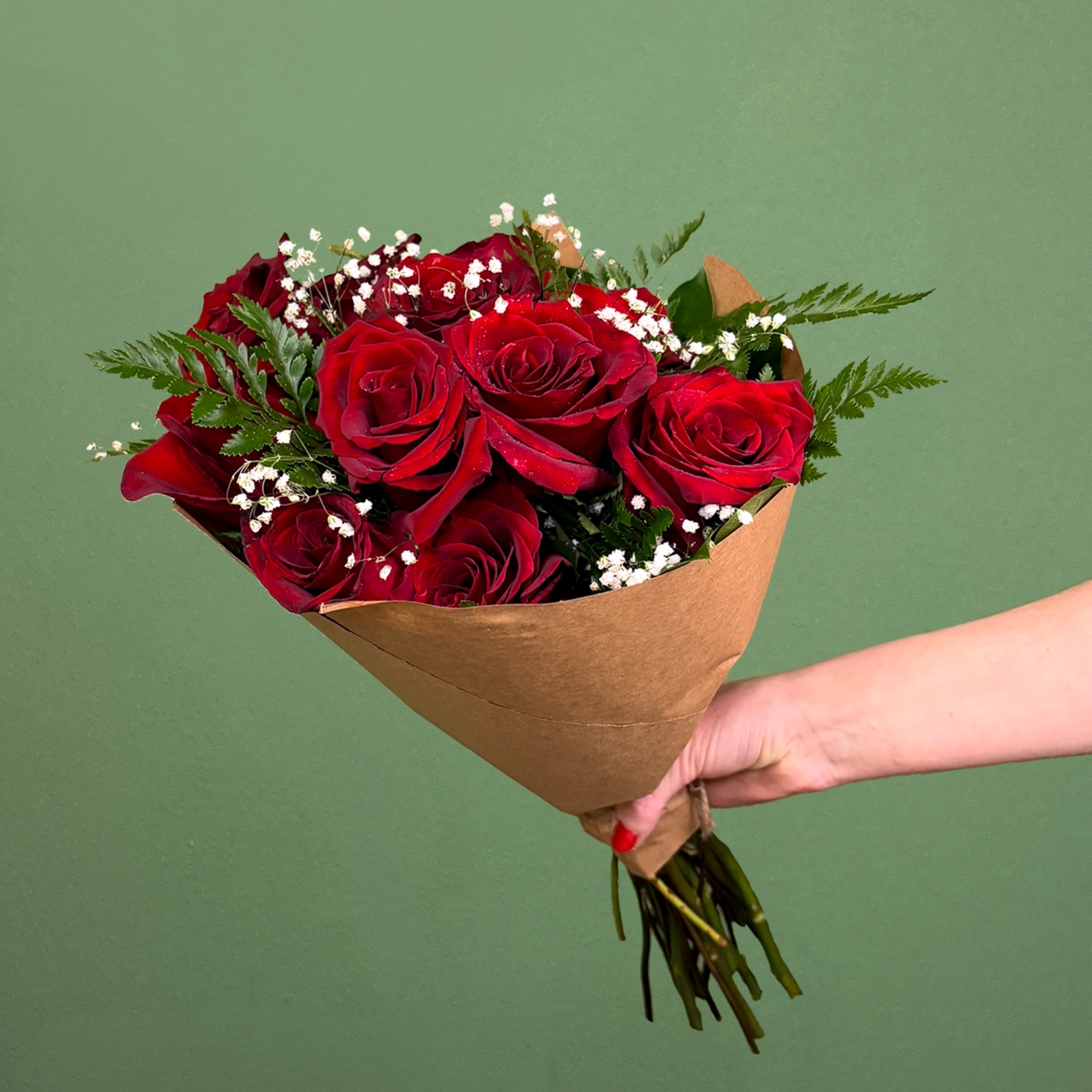 Handheld bouquet of red roses wrapped in brown paper against a green background