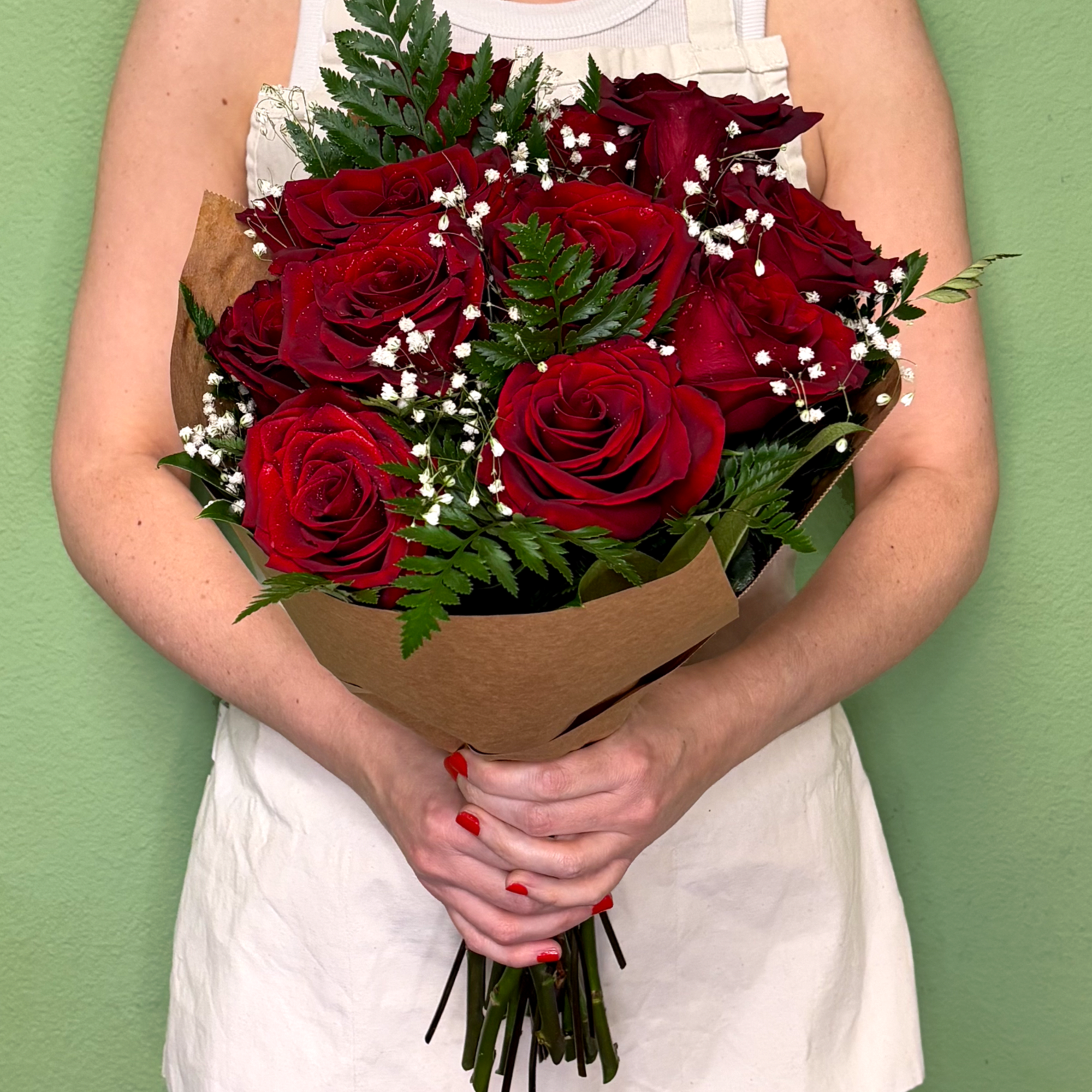 Hand-tied bouquet of red roses with white filler flowers wrapped in brown paper