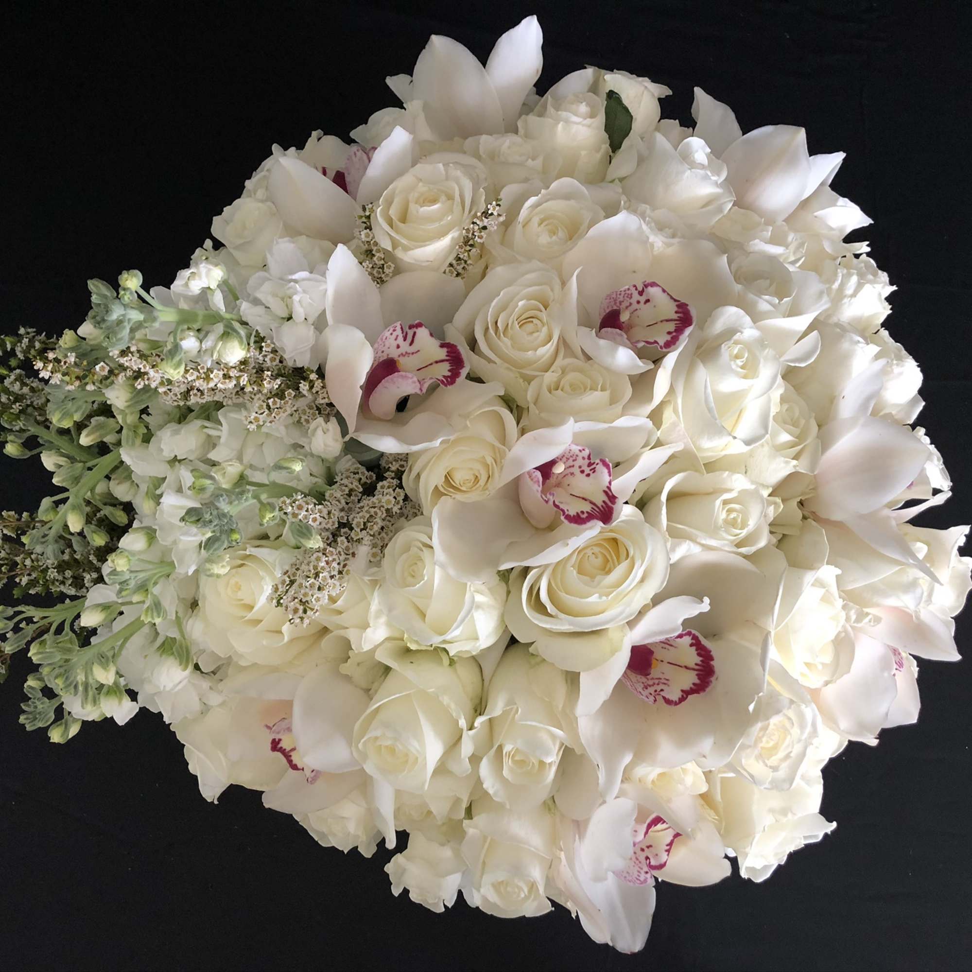 White rose and orchid bouquet with trailing greenery on a black background