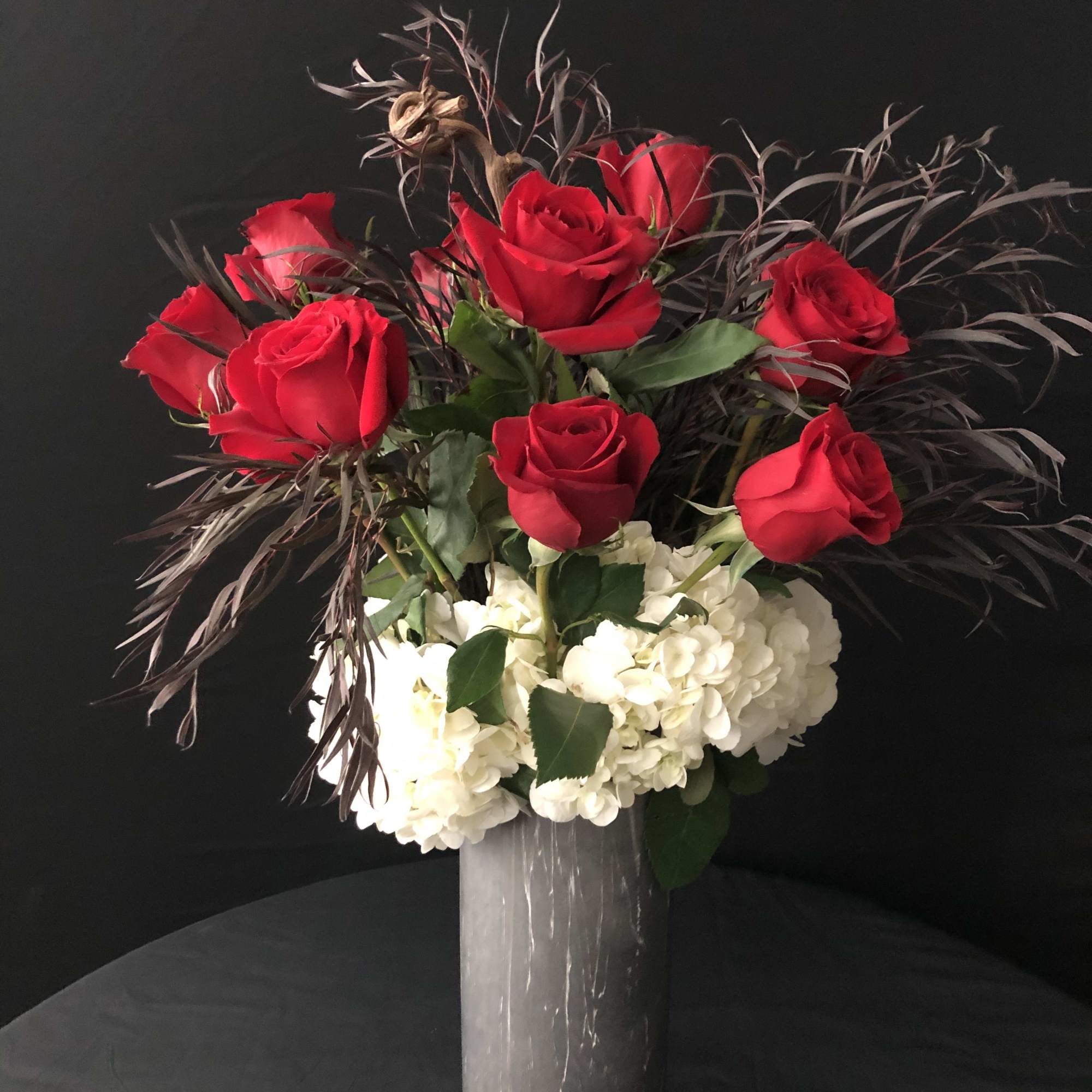 Red roses arranged with white hydrangeas in a tall vase