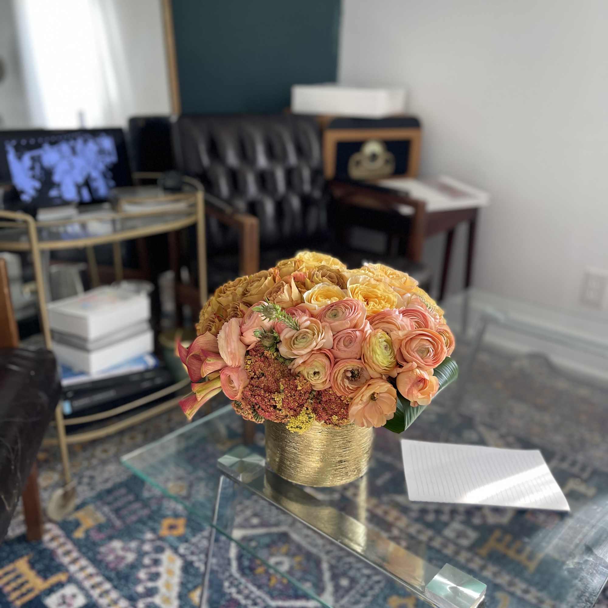 Peach and yellow flower arrangement in a gold vase on a glass table