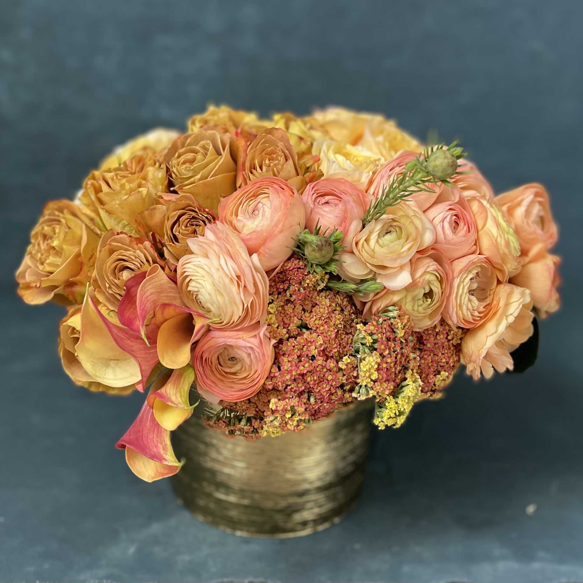 Peach and yellow bouquet with calla lilies in a gold vase