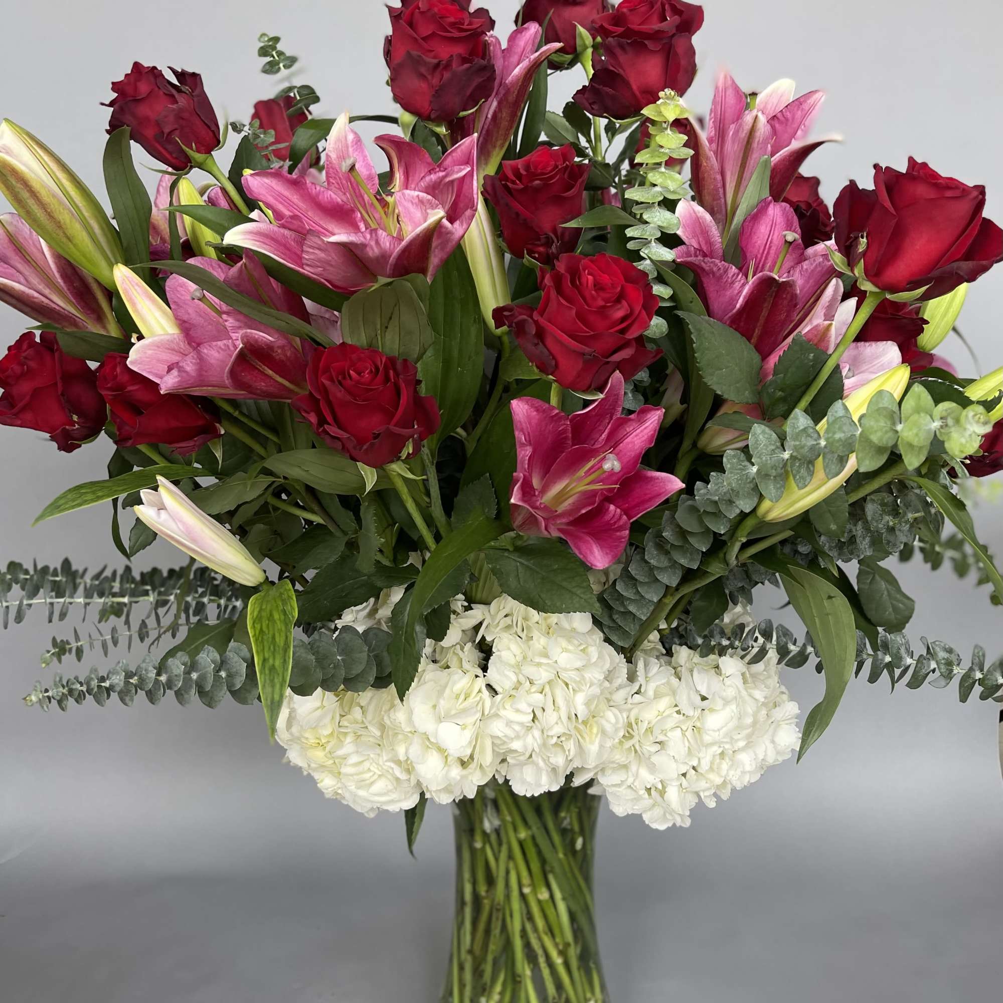 Bouquet of red roses, pink lilies, and white hydrangeas in a glass vase