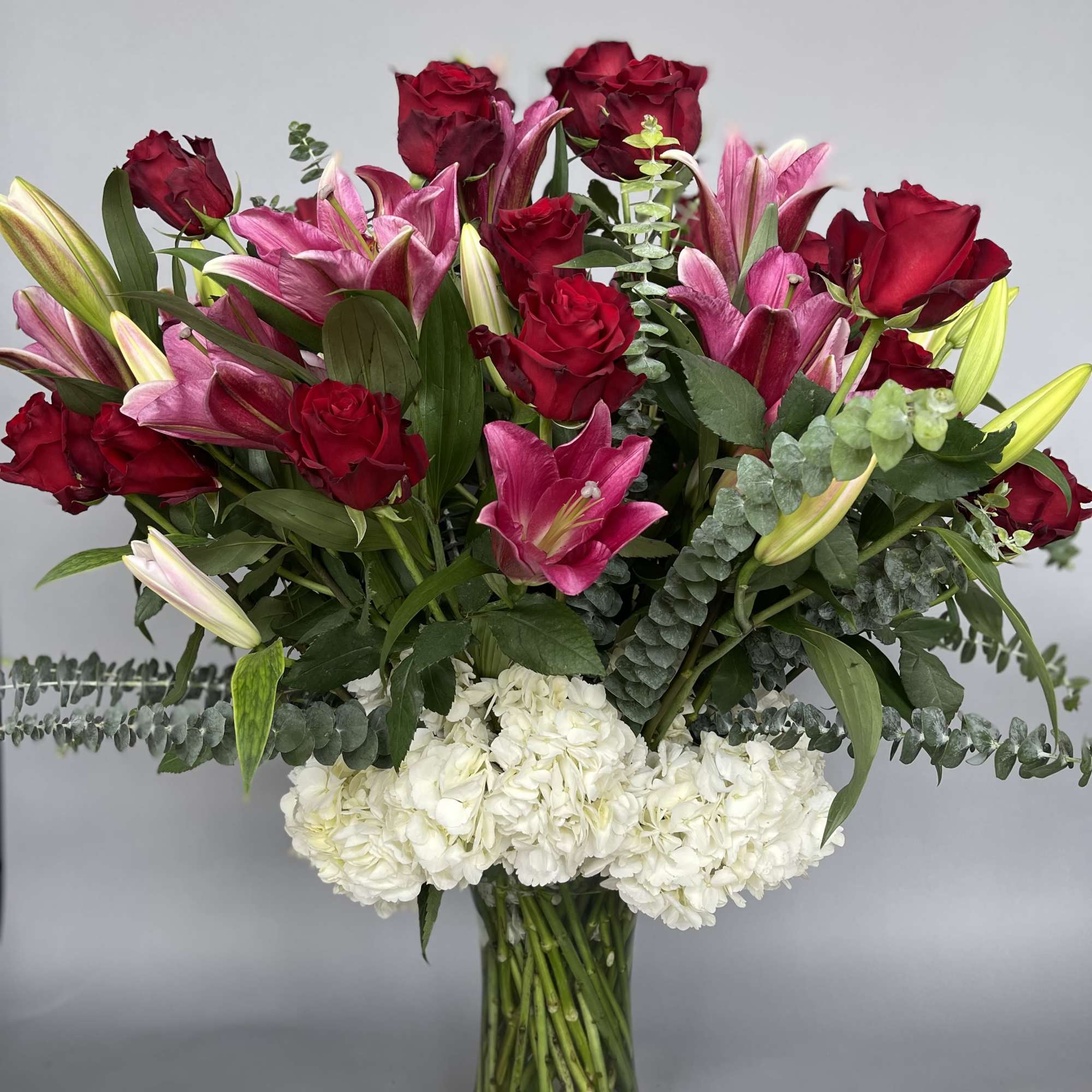 Red roses and pink lilies arranged in a clear glass vase with white hydrangeas.