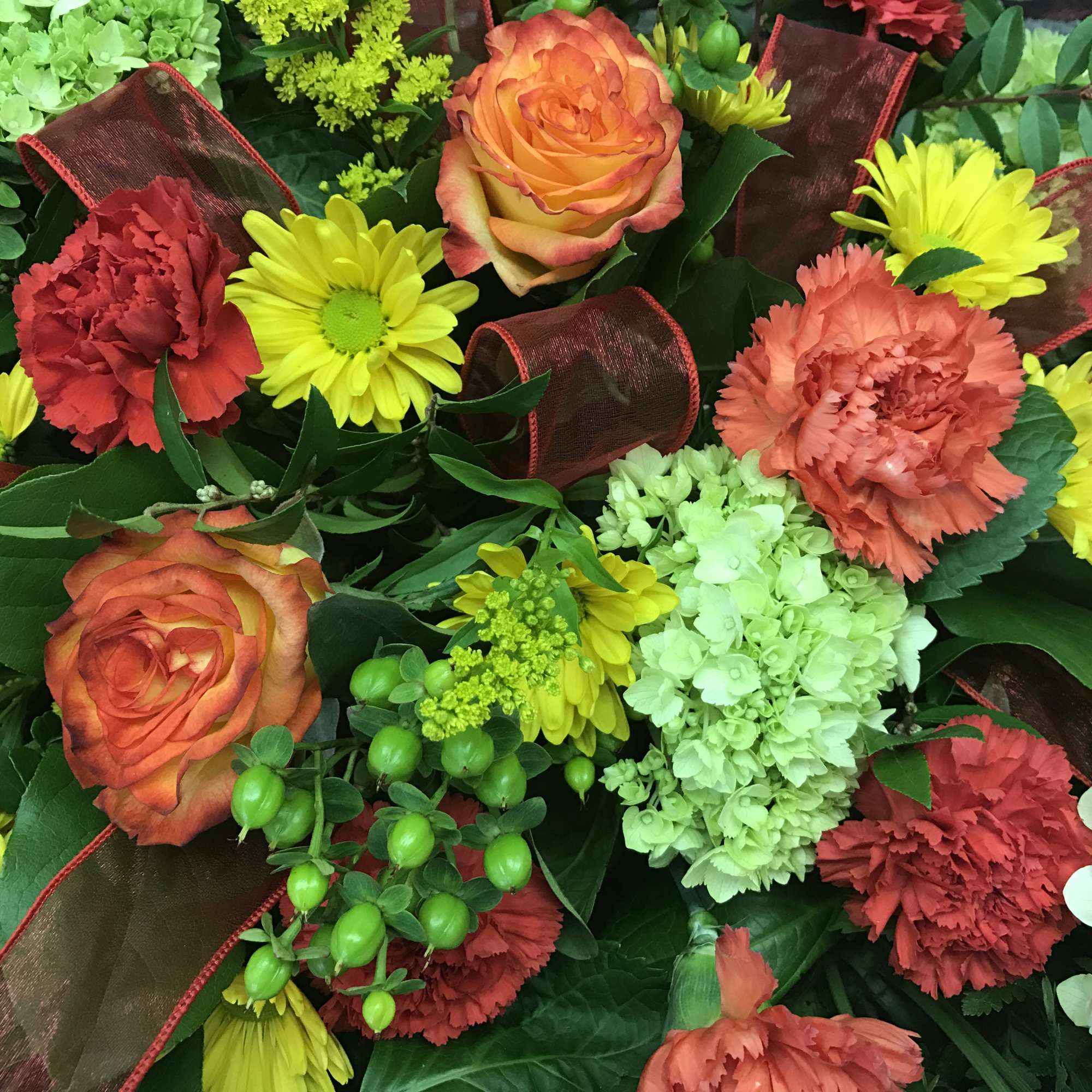 Bouquet of orange roses, red carnations, yellow daisies, and green hydrangea
