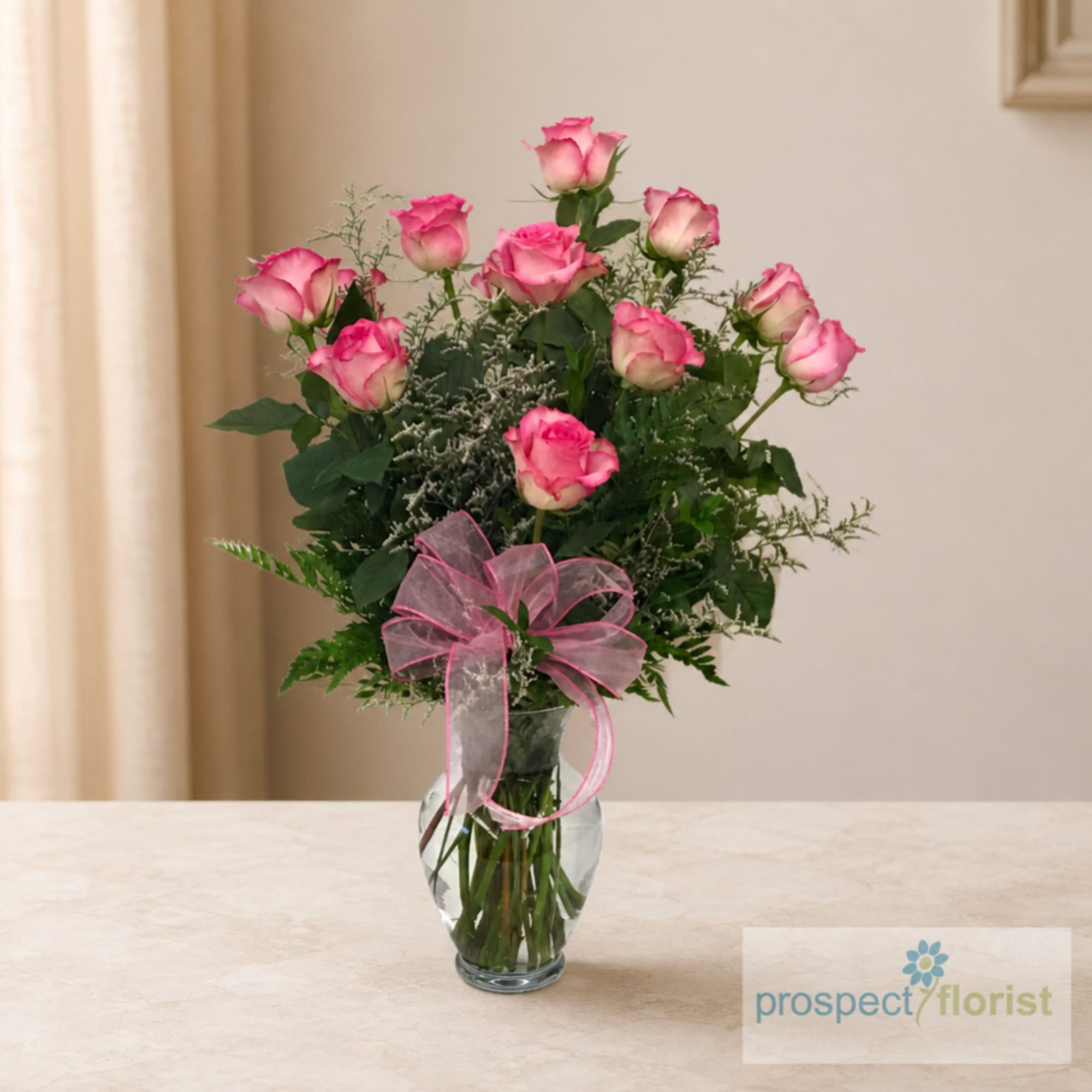 Pink roses arranged in a clear glass vase with a pink ribbon bow