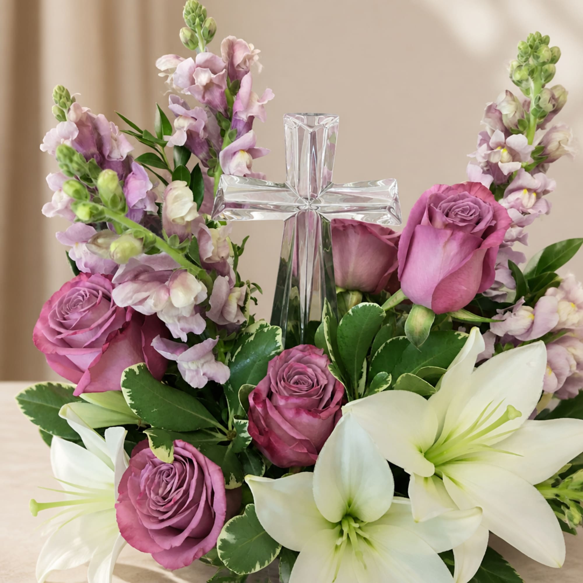 Purple roses and white lilies arranged around a clear glass cross