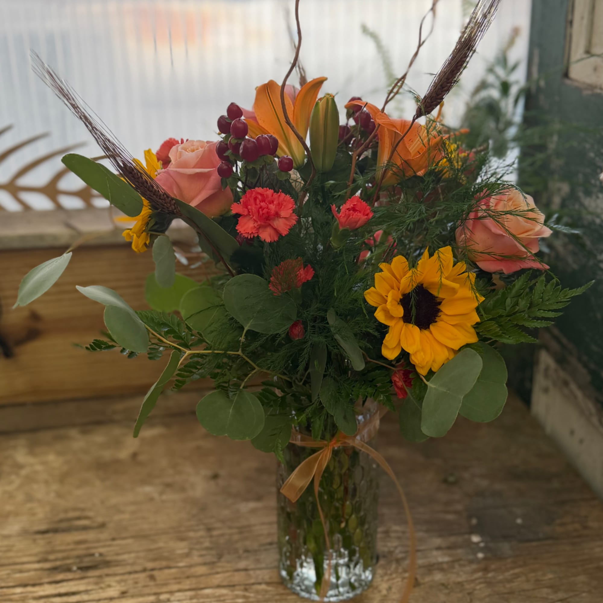 Mixed bouquet with roses, sunflowers, lilies, and carnations in a glass vase
