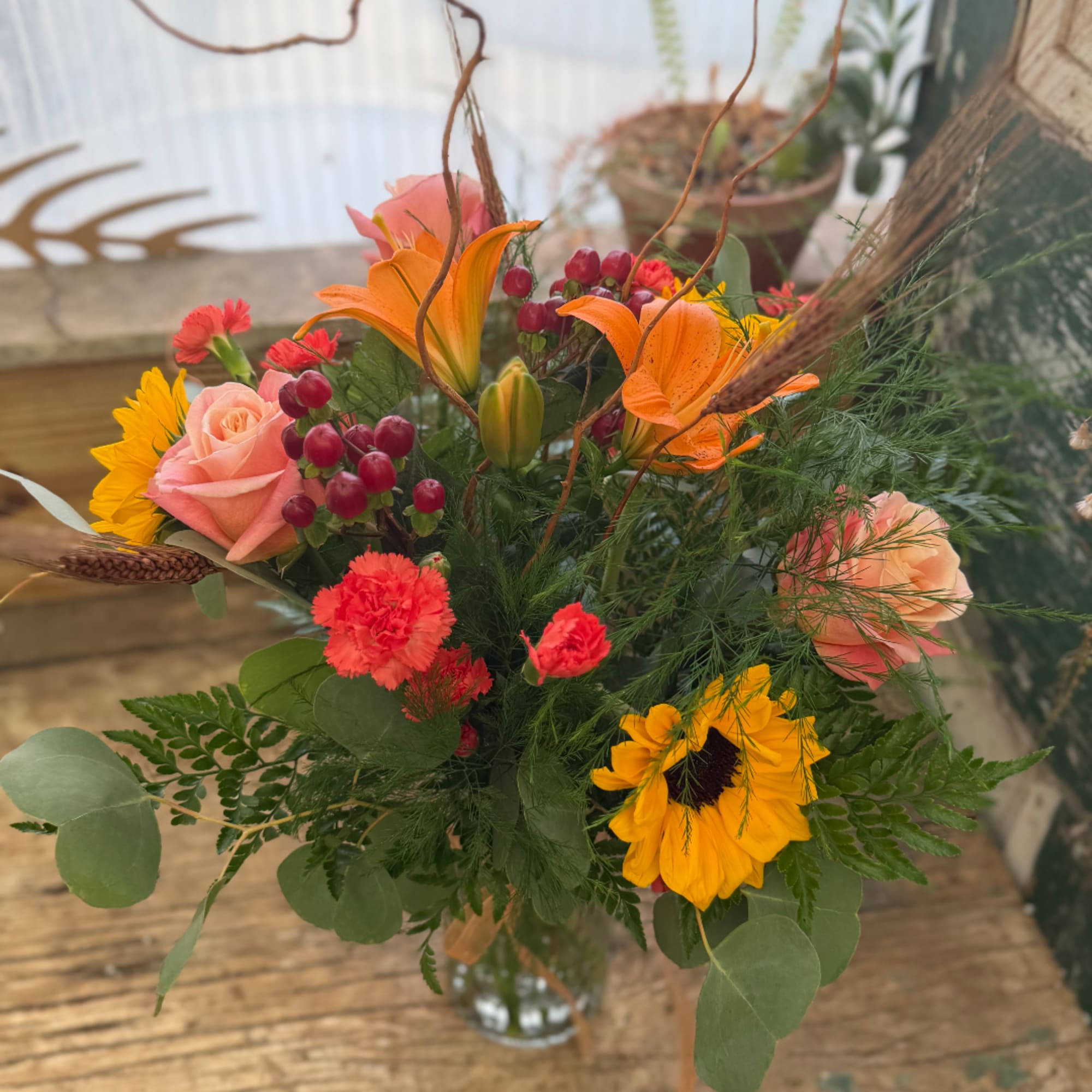 Mixed bouquet with orange lilies, pink roses, and yellow sunflowers in a glass vase