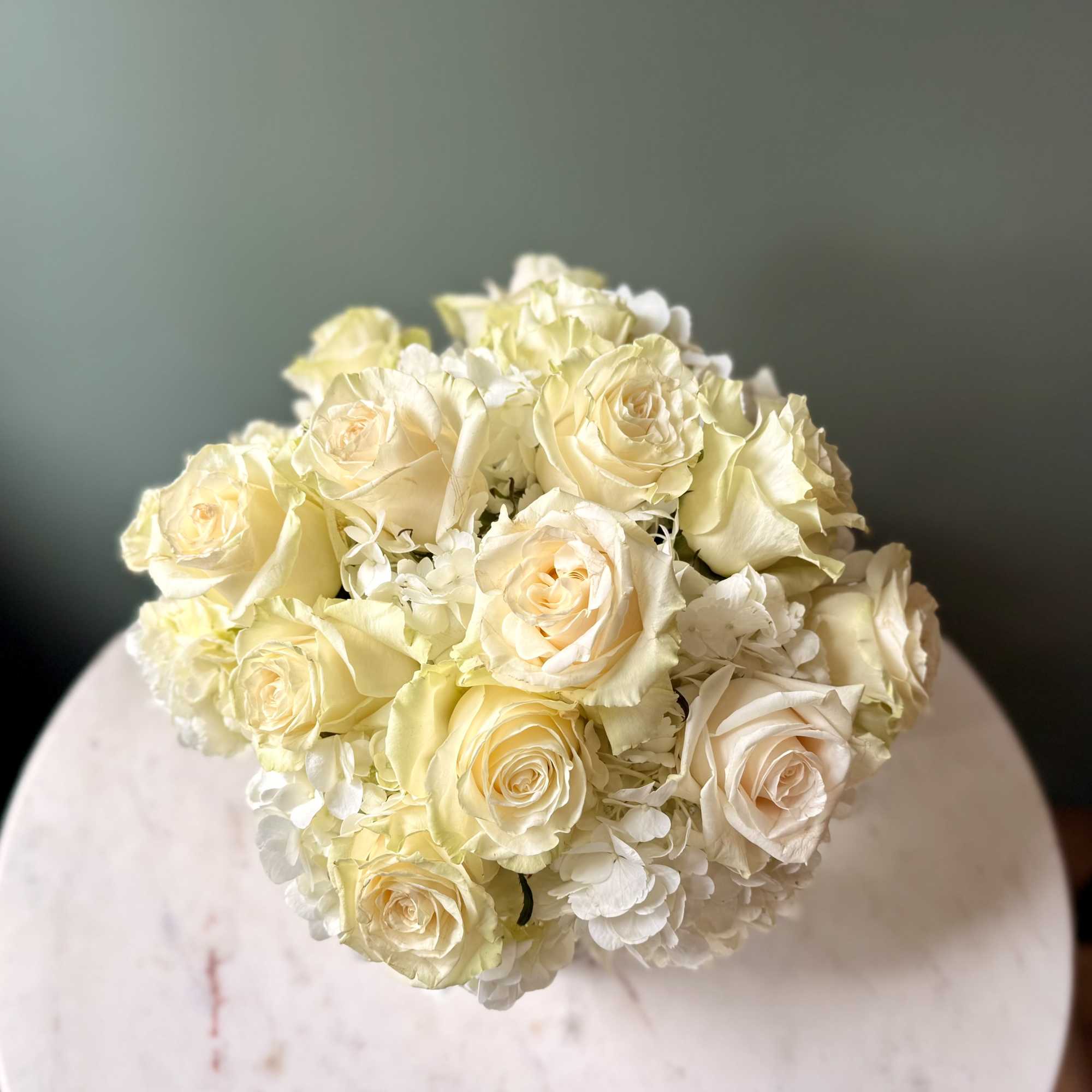 Compact arrangement of ivory roses and white hydrangeas viewed from above on a round white table